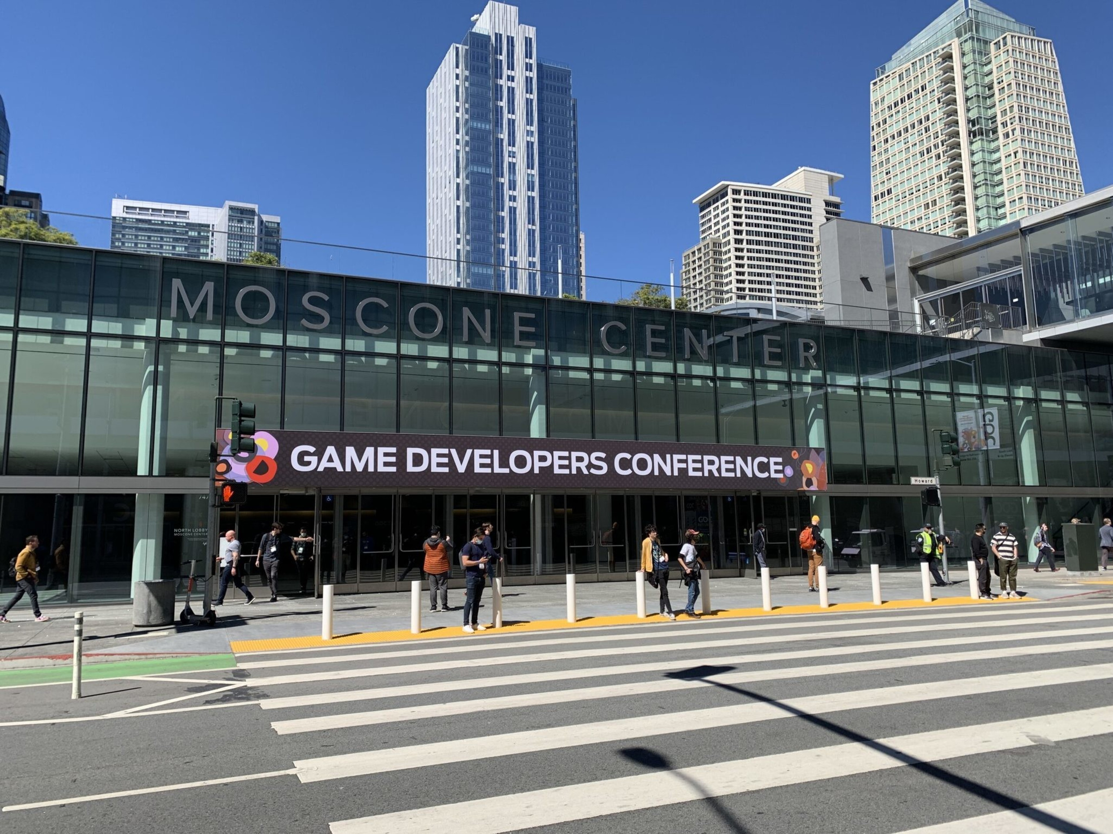 Moscone Center building with people standing outside and a digital sign reading "Game Developers Conference" above the entrance under a clear blue sky.