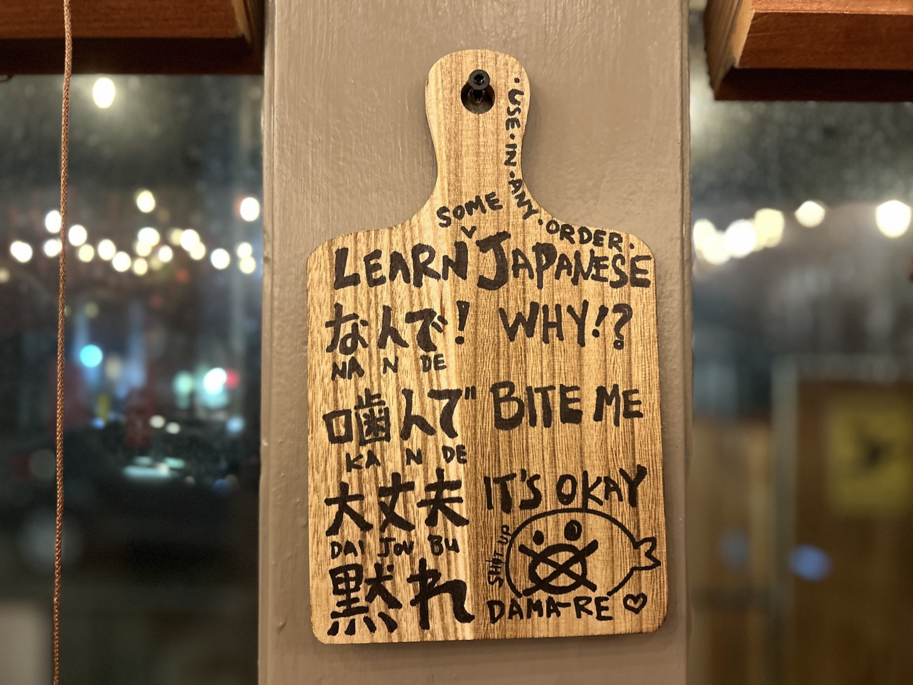 a wall-mounted paddle with translations of tongue-in-cheek Japanese phrases