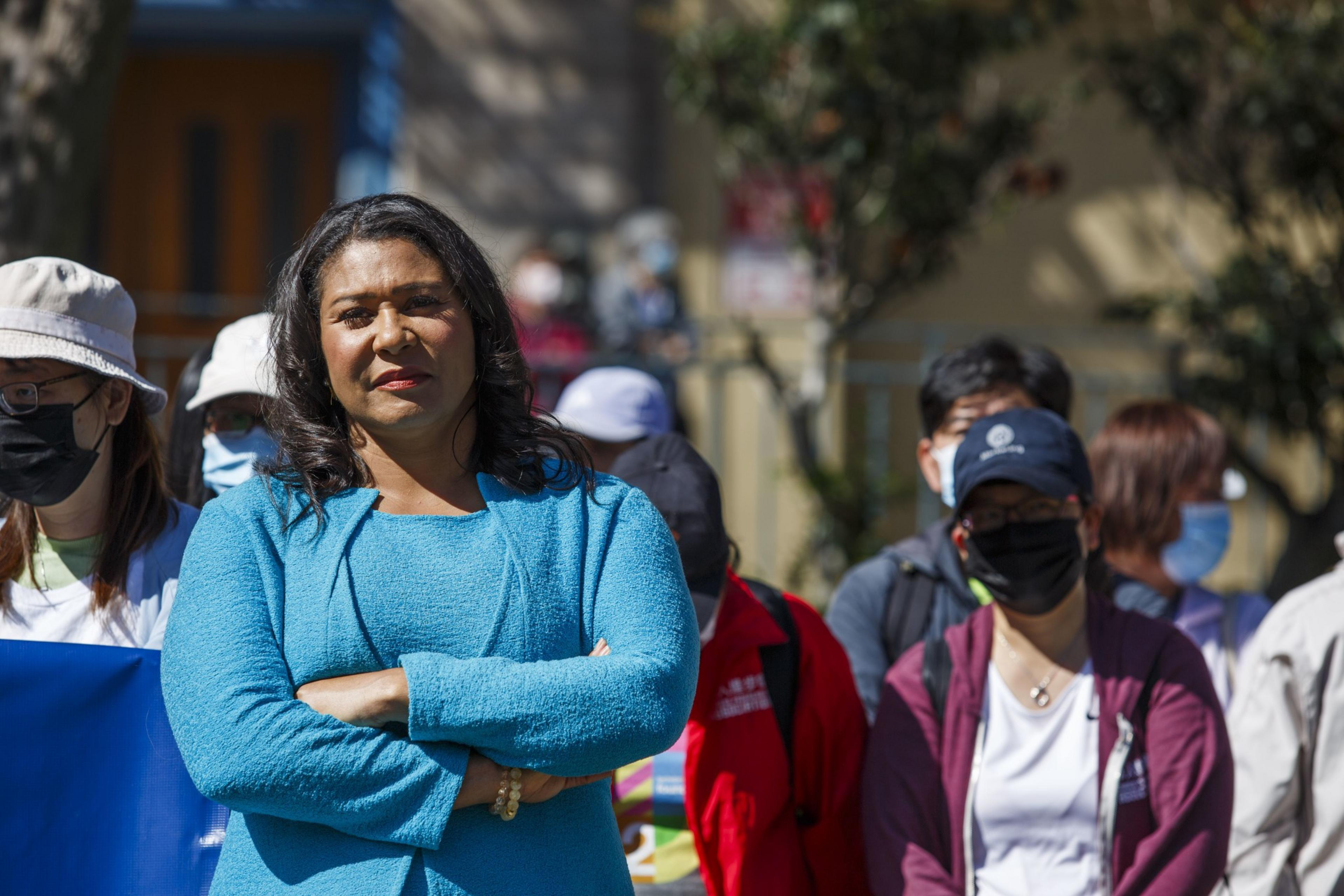 A woman with crossed arms stands out in a crowd of masked people.