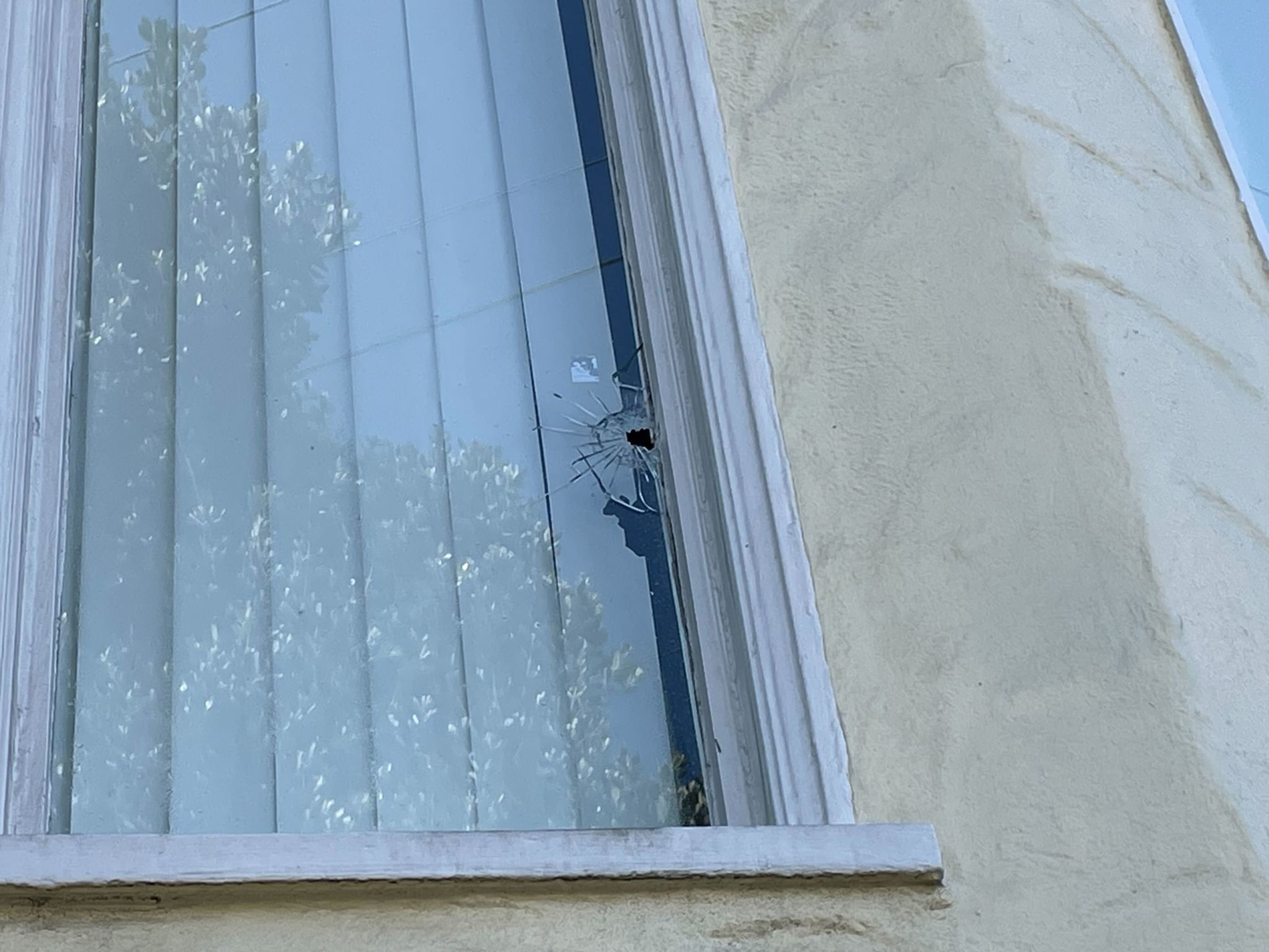 A window with a cracked pane and patterned curtain, set in a textured beige wall.