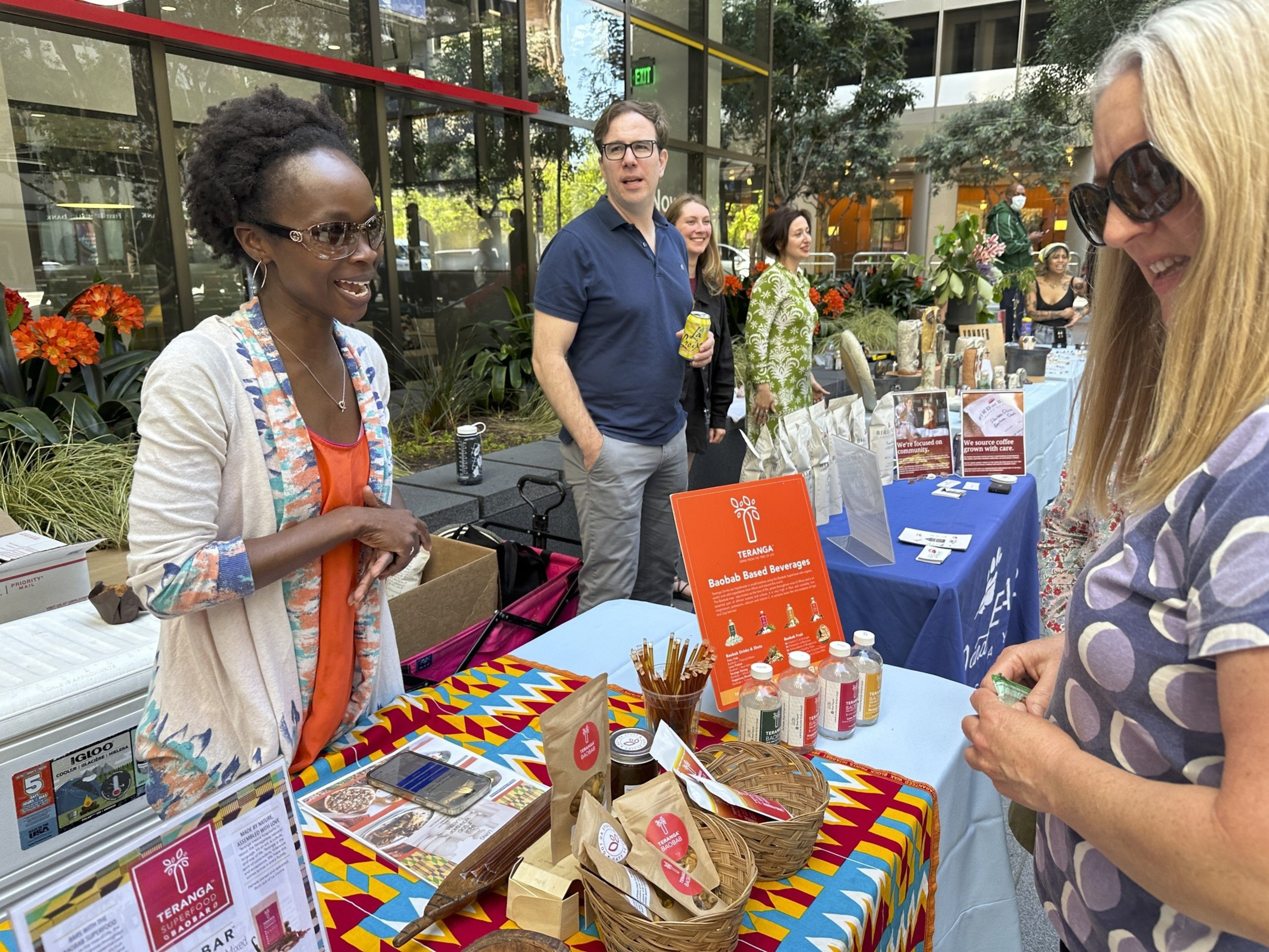 A woman at a stand talks with a another woman about a suite of color bar and juice products.