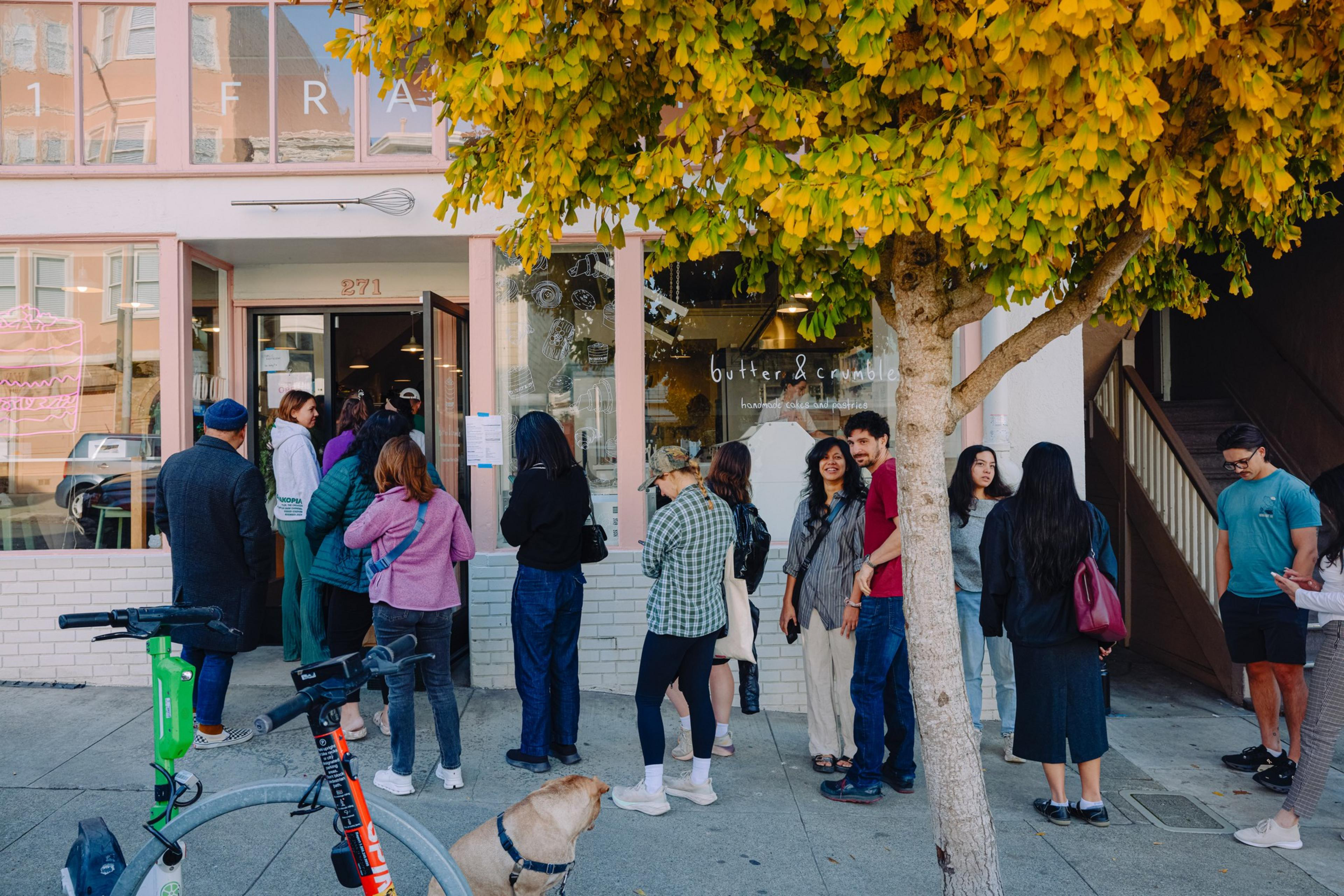 A bakery storefront with a line of people waiting outside.