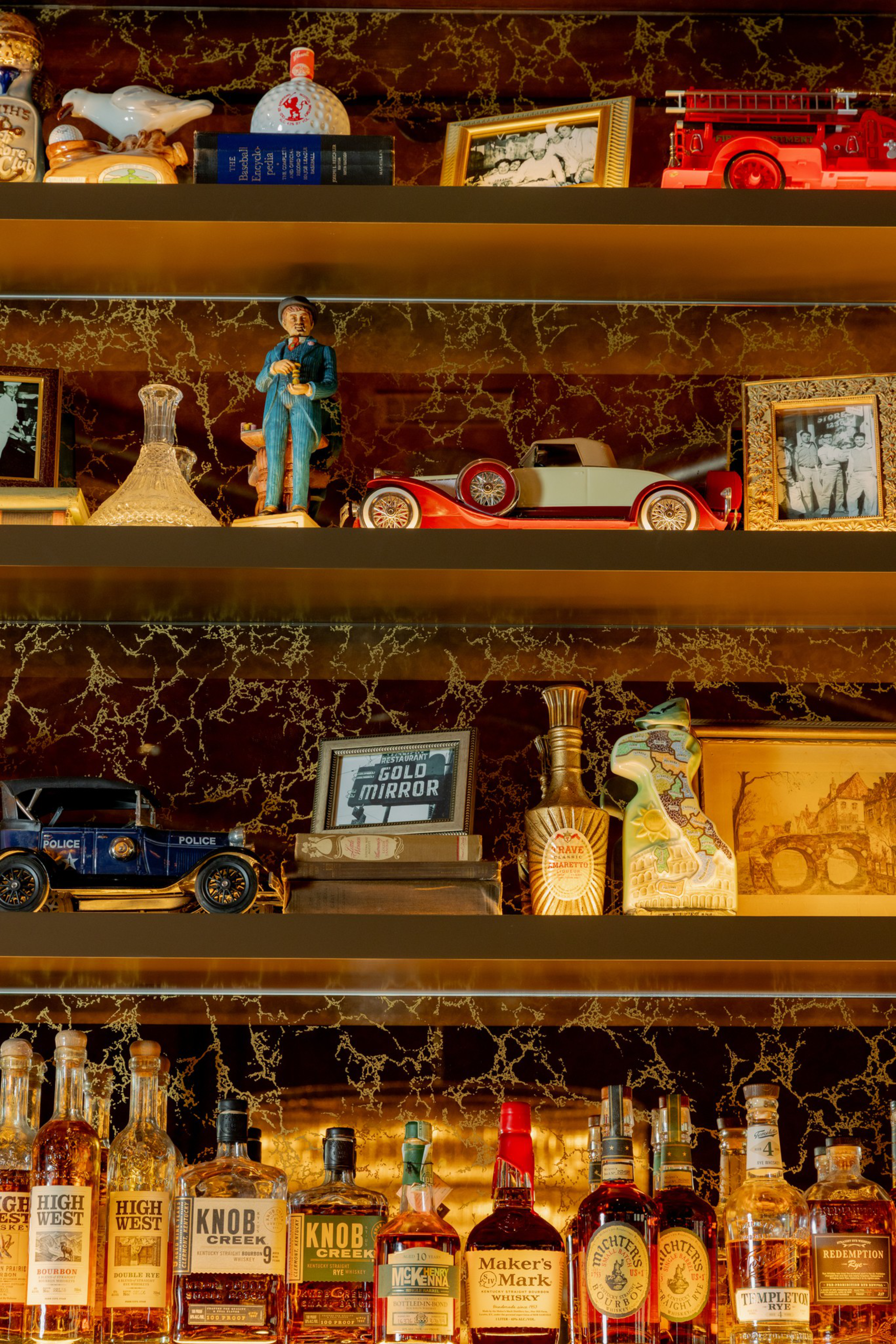 Shelves with vintage decor including framed photos, toy cars, figurines, glassware, and bottles of various whiskeys and spirits.