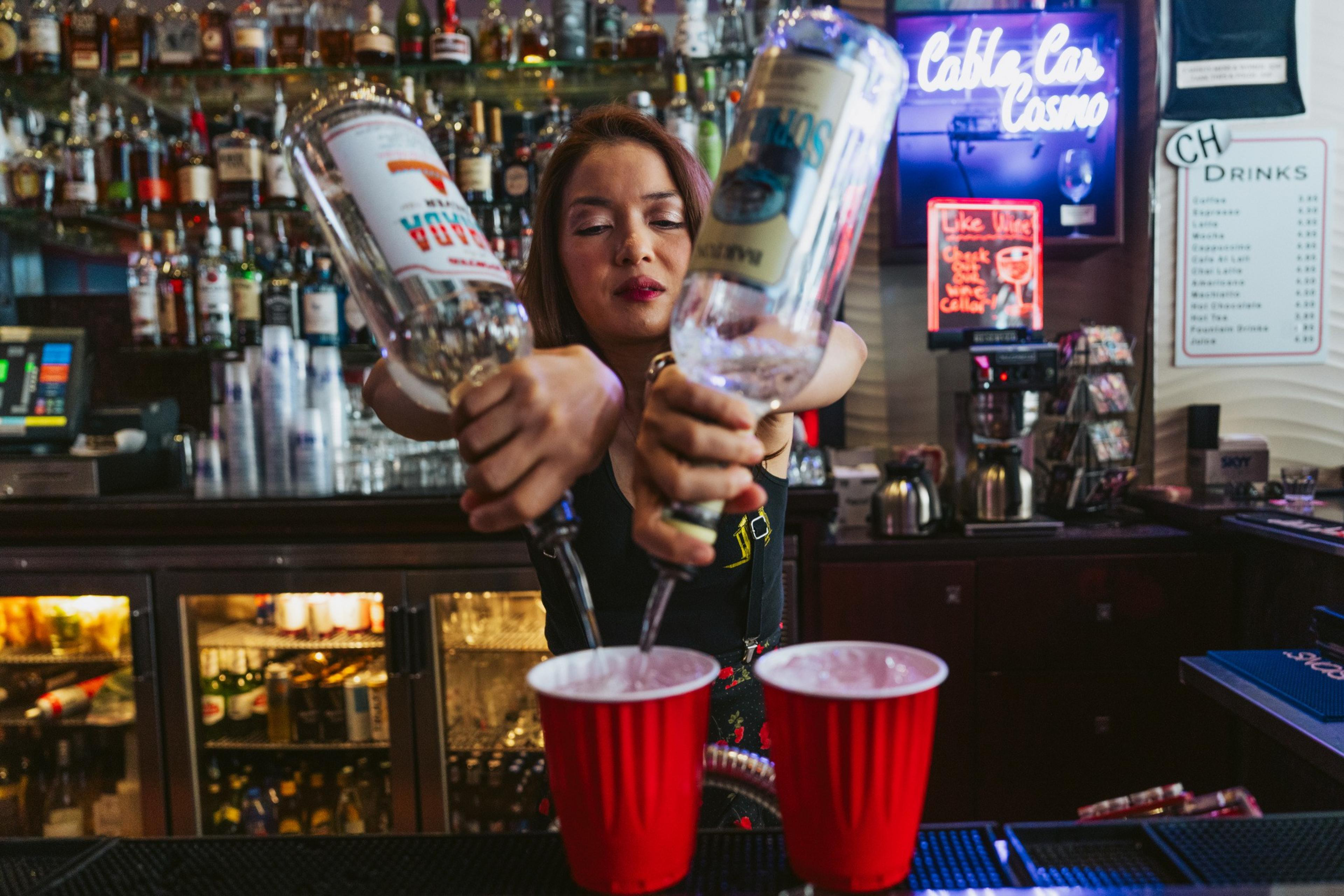 A bartender pours two bottles of liquor into a red plastic cup.