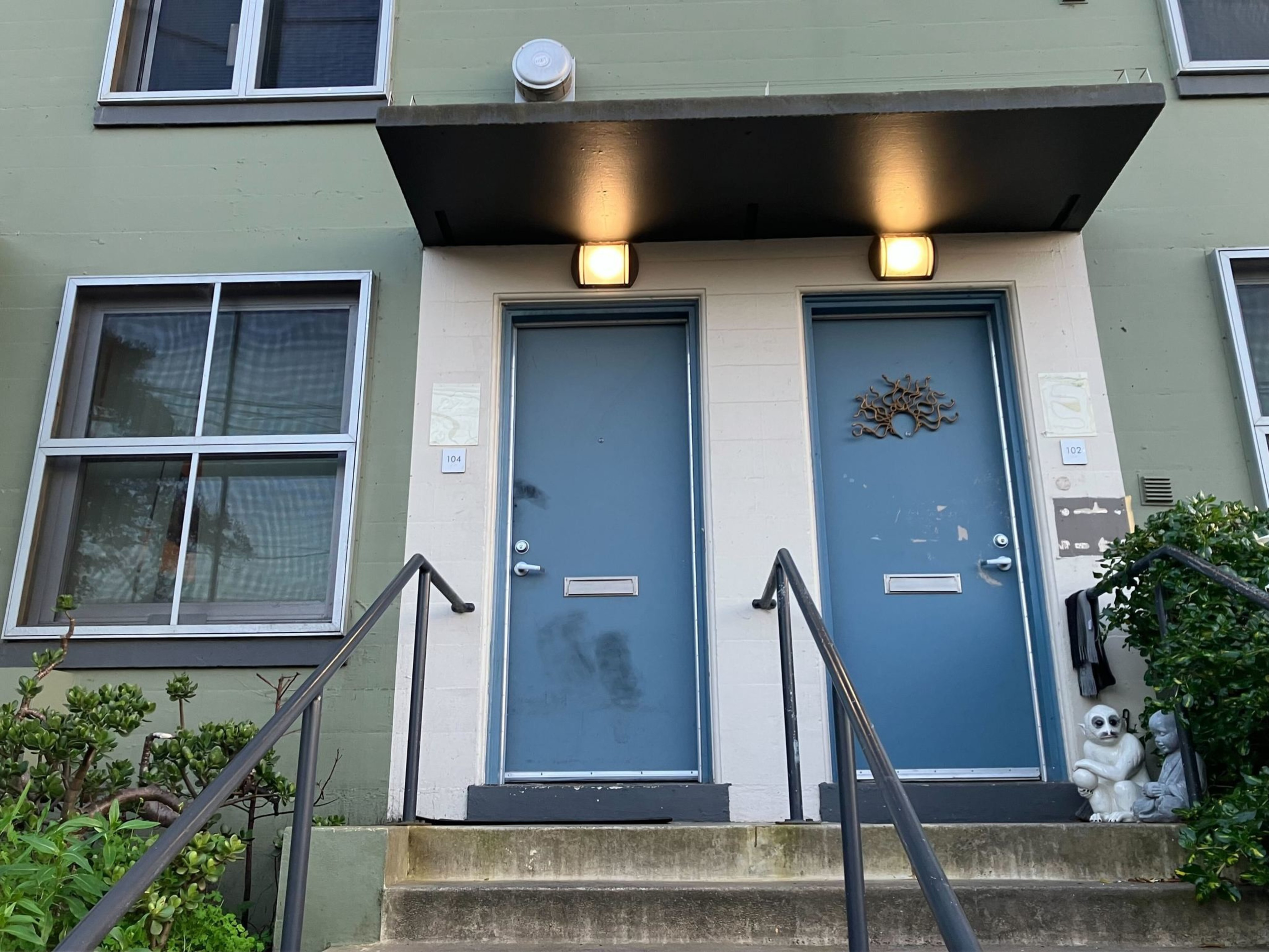 Two blue doors of a green building with a metal railing, lights above each door, and a dog statue to the right.