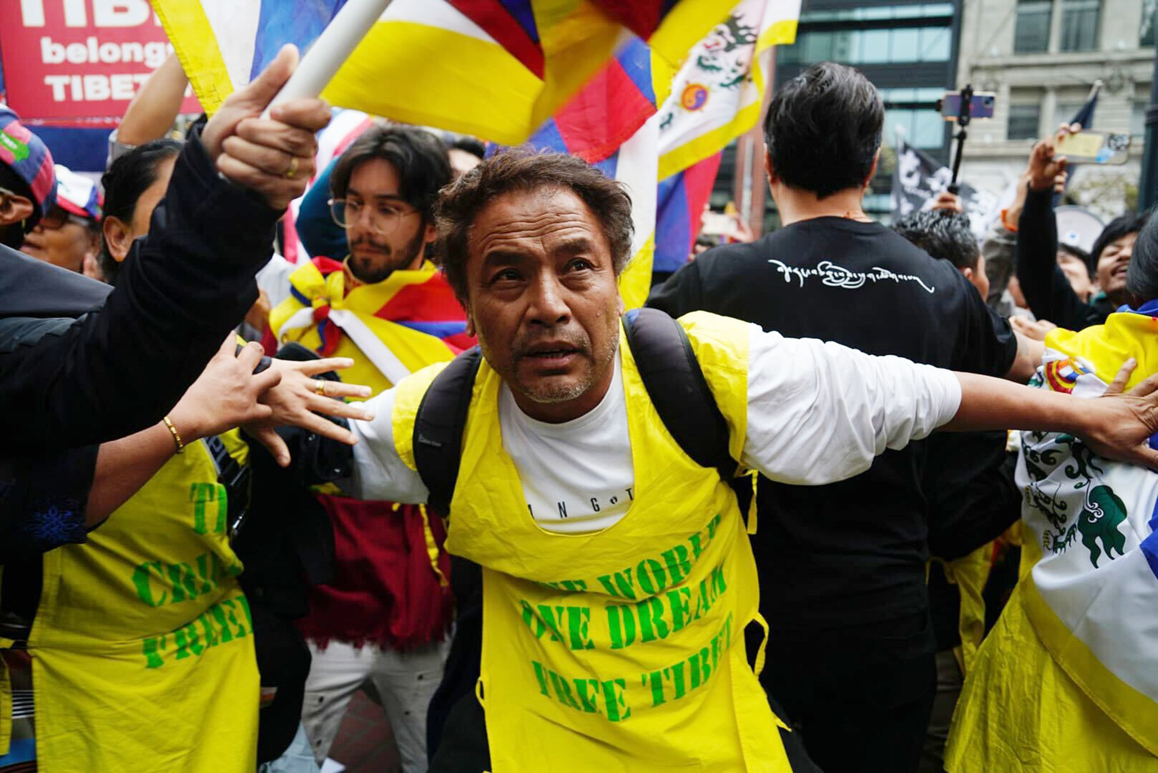 A man looks into the distance during a protest with Tibetan flags in the background.