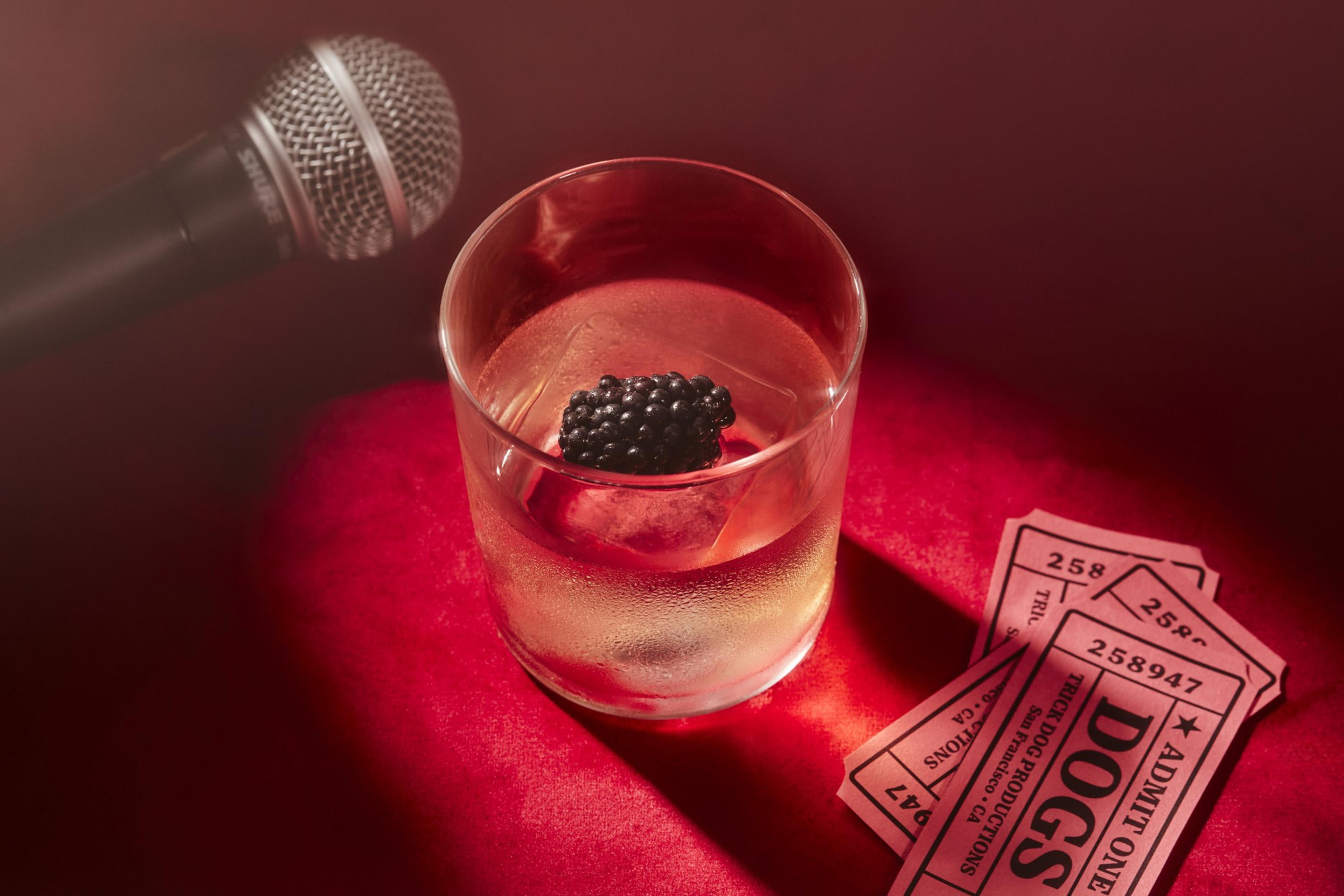 A microphone, a drink with ice and a blackberry, and three red &quot;Admit One&quot; tickets lie on a red surface.