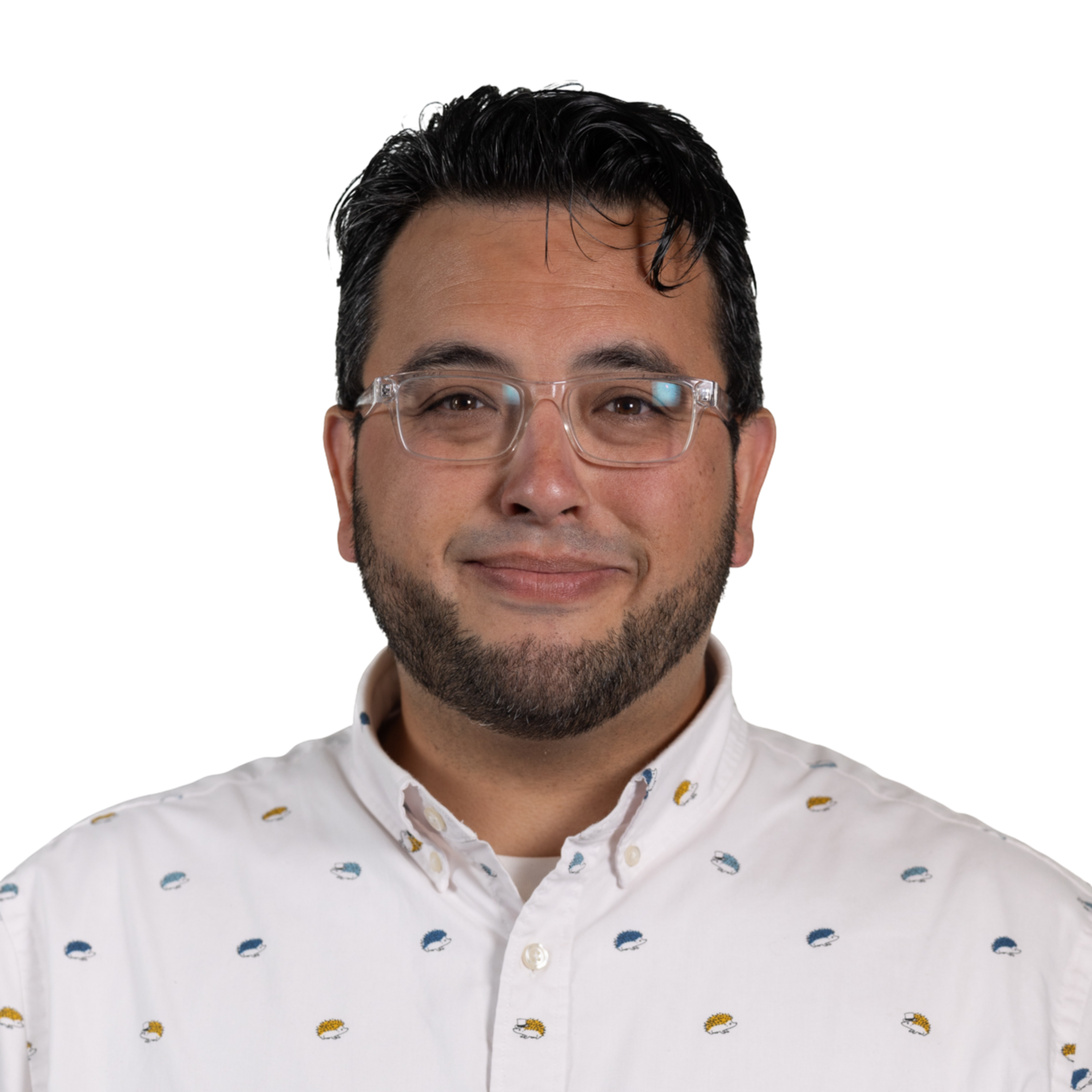 A man with short dark hair, clear glasses, and a trimmed beard smiles softly, wearing a white button-up shirt with small multicolored patterns.