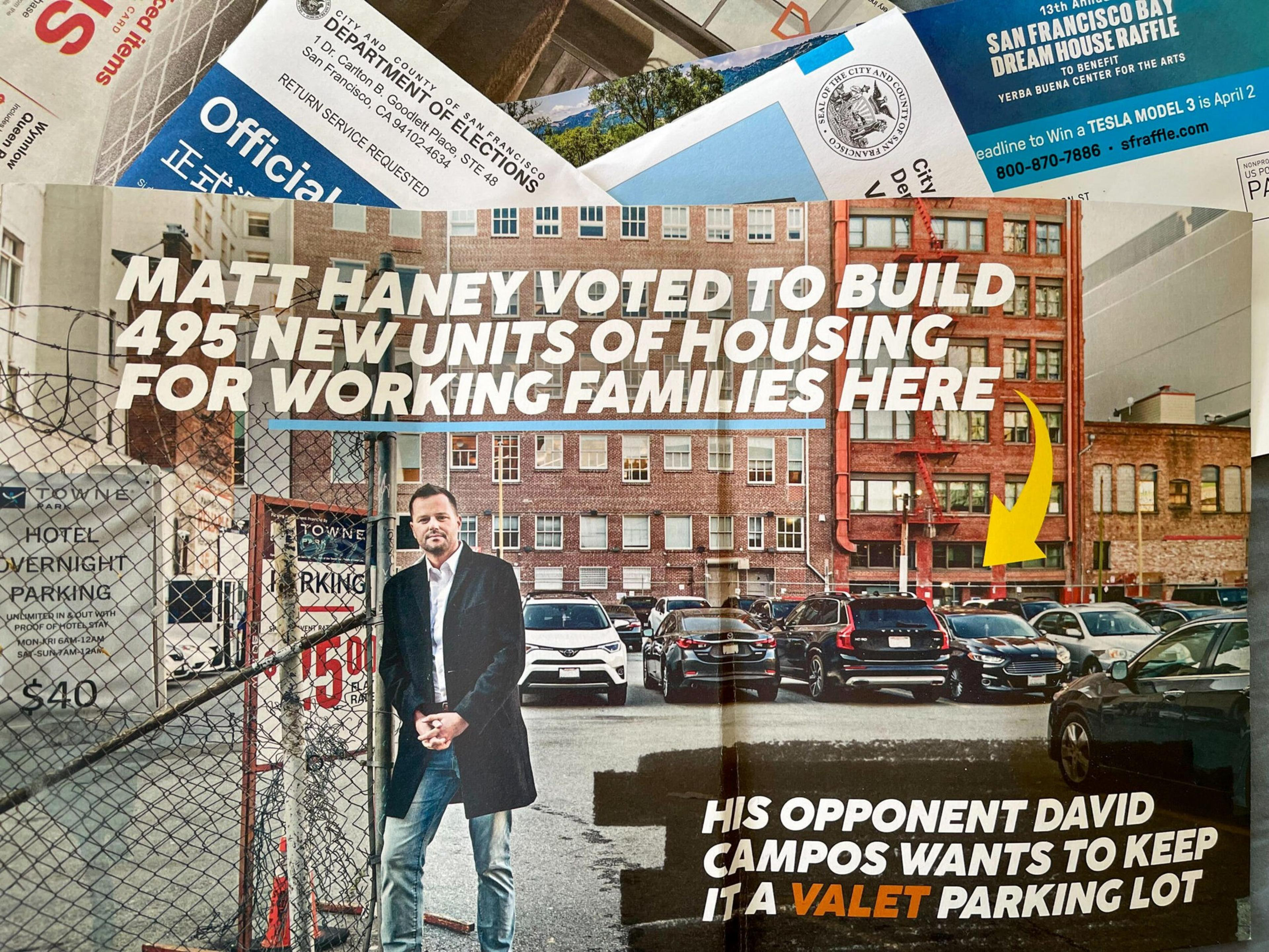 Matt Haney stands in front of a fenced parking lot with multiple parked cars and brick buildings, promoting housing over maintaining a valet parking lot.