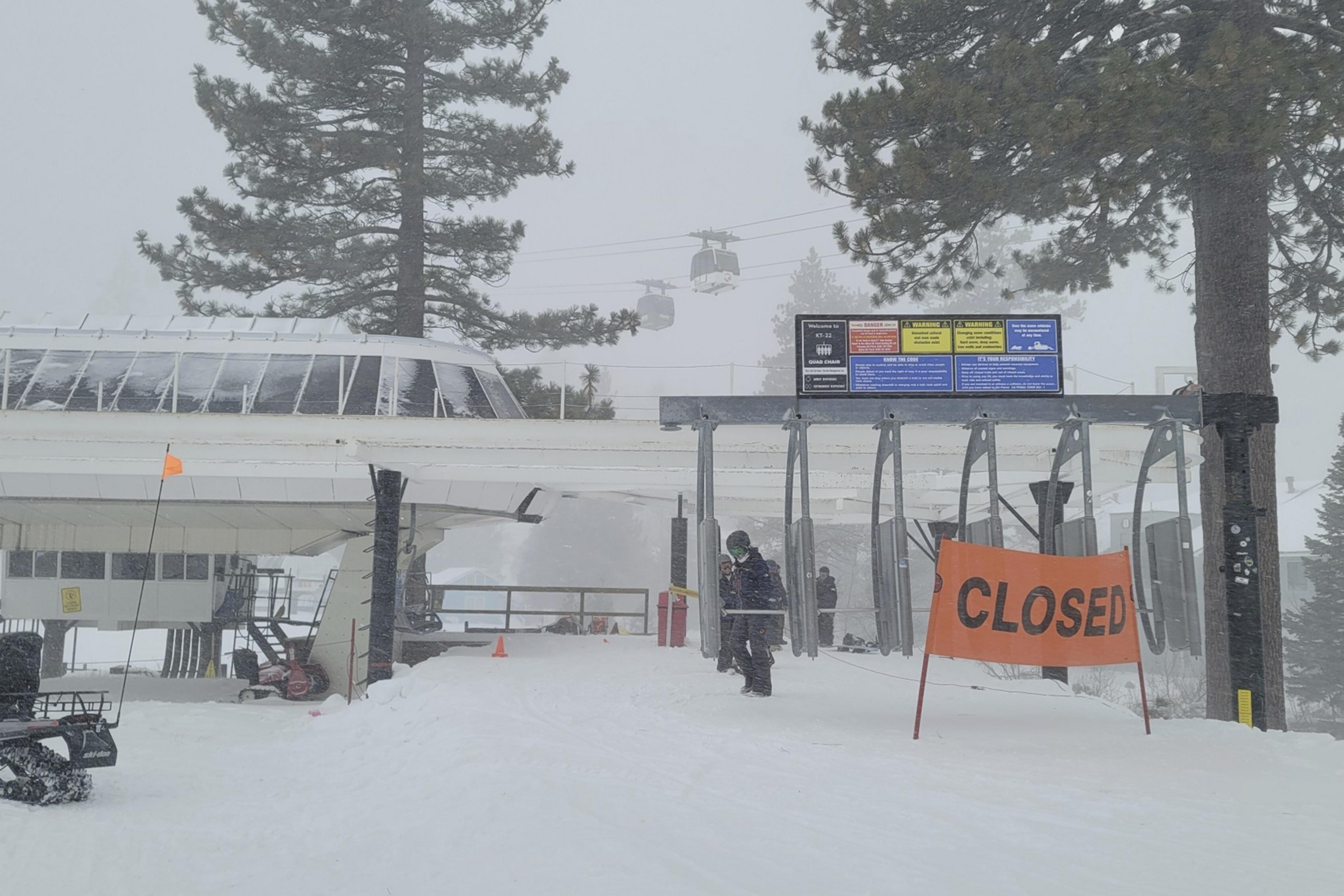 An orange closed sign sticks out of the snow in front of a ski chair lift