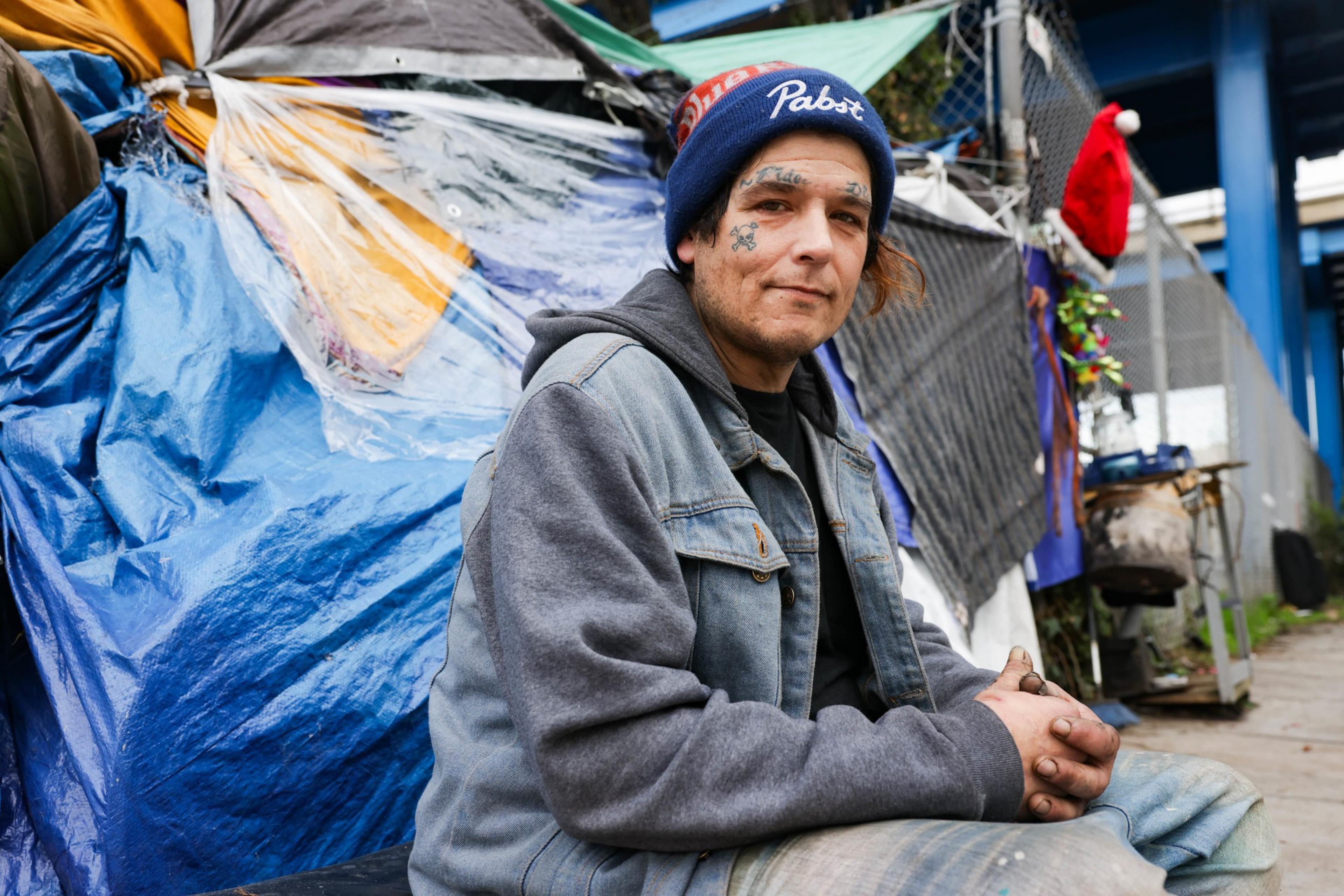 A person sits on the ground right next to tents on the street.