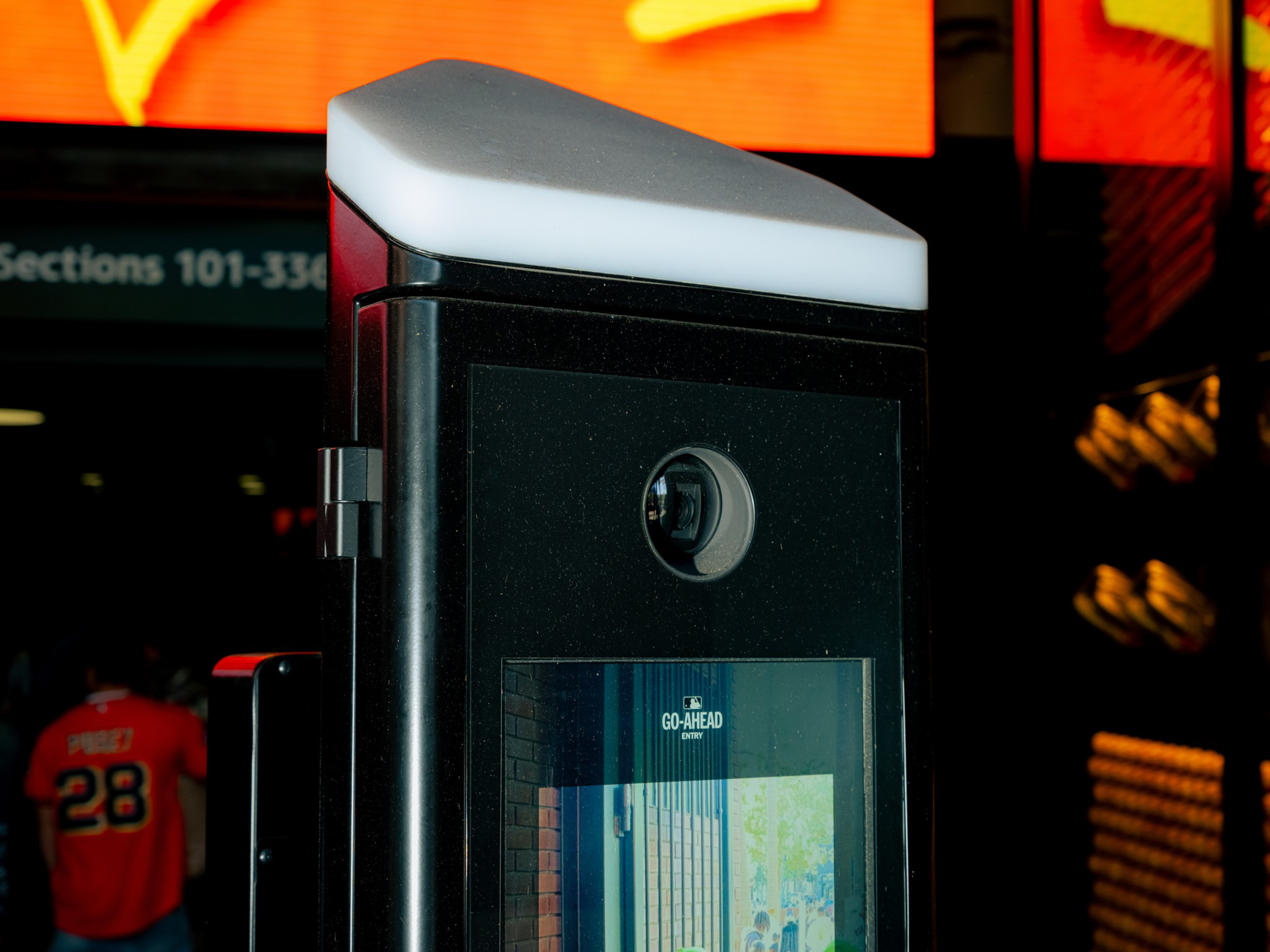 A black, rectangular device with a camera lens and a screen displaying the words “GO-AHEAD” stands in front of a person wearing an orange jersey with the number 28.