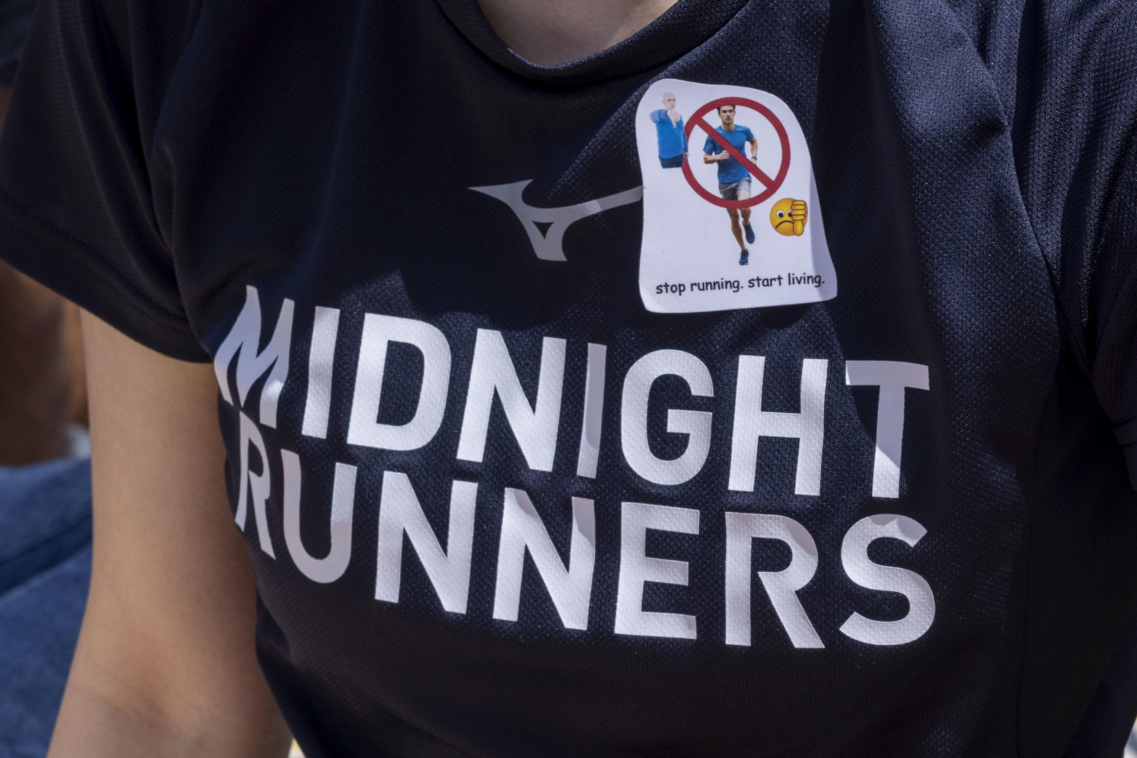 The image shows a person wearing a dark &quot;Midnight Runners&quot; shirt with a sticker saying &quot;stop running, start living,&quot; featuring a crossed-out runner and a thumbs-down emoji.