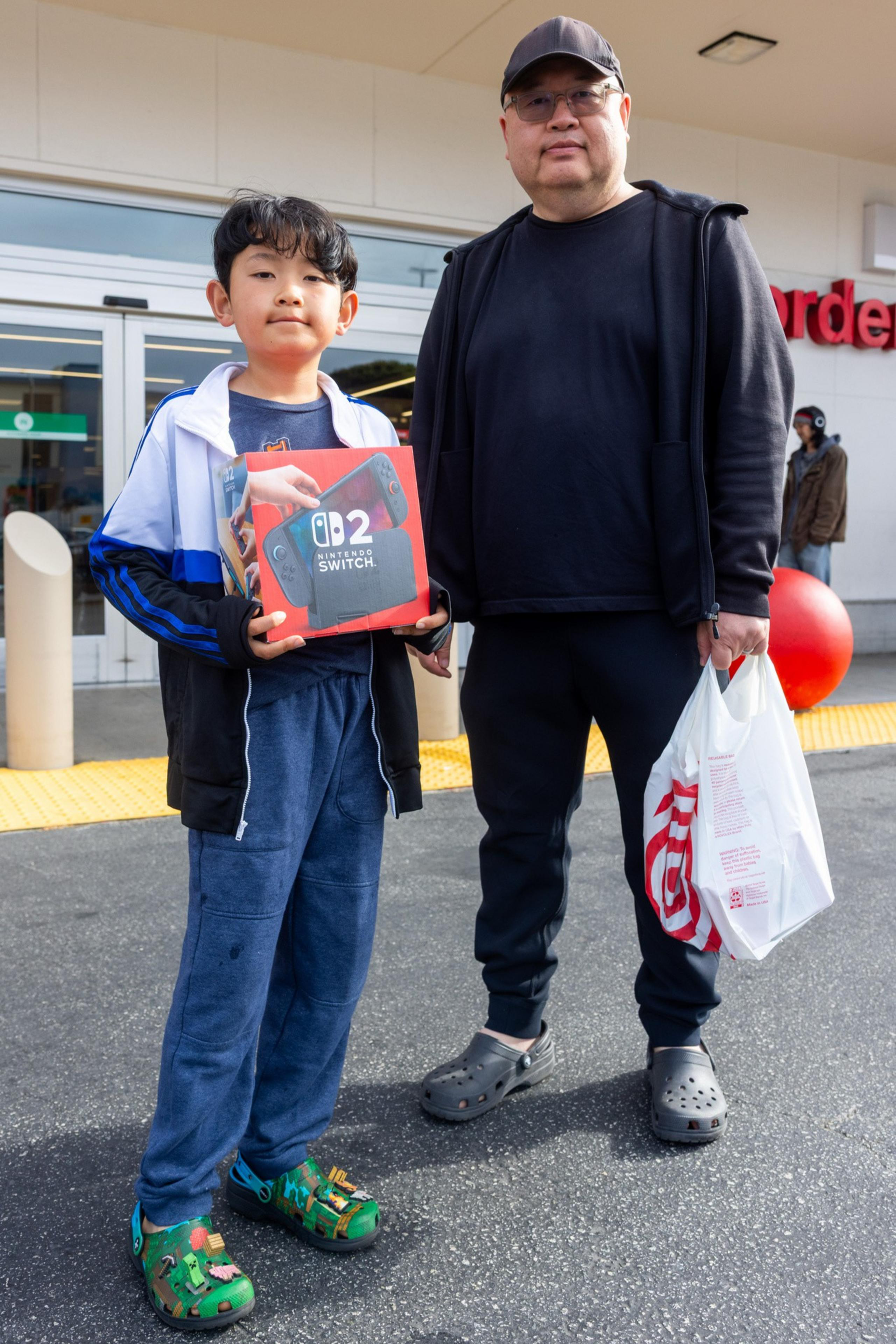 A child holding a Nintendo Switch OLED box stands beside an adult with a Target bag, both in casual clothing, outside a store with the Target logo visible.