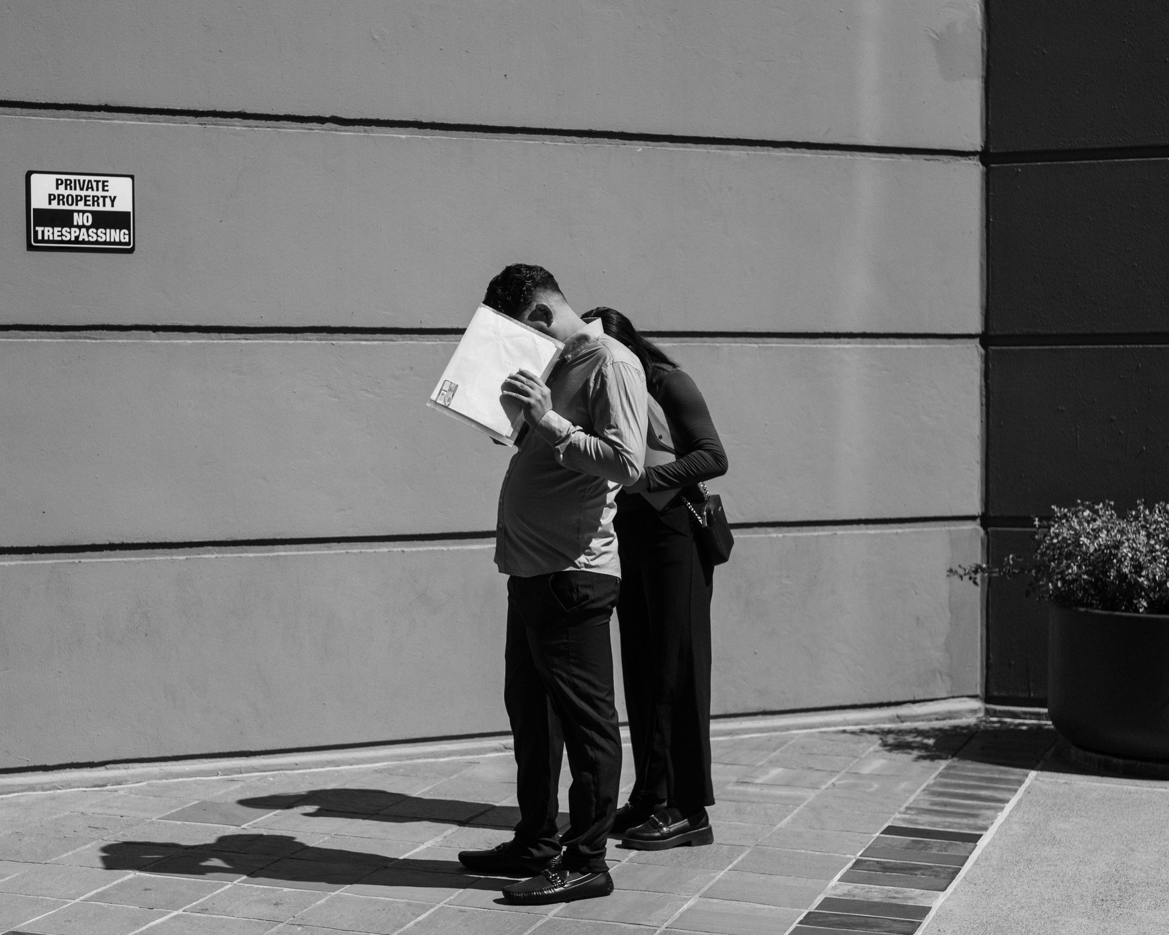 A man covers his face with a paper while standing close to a woman who ...