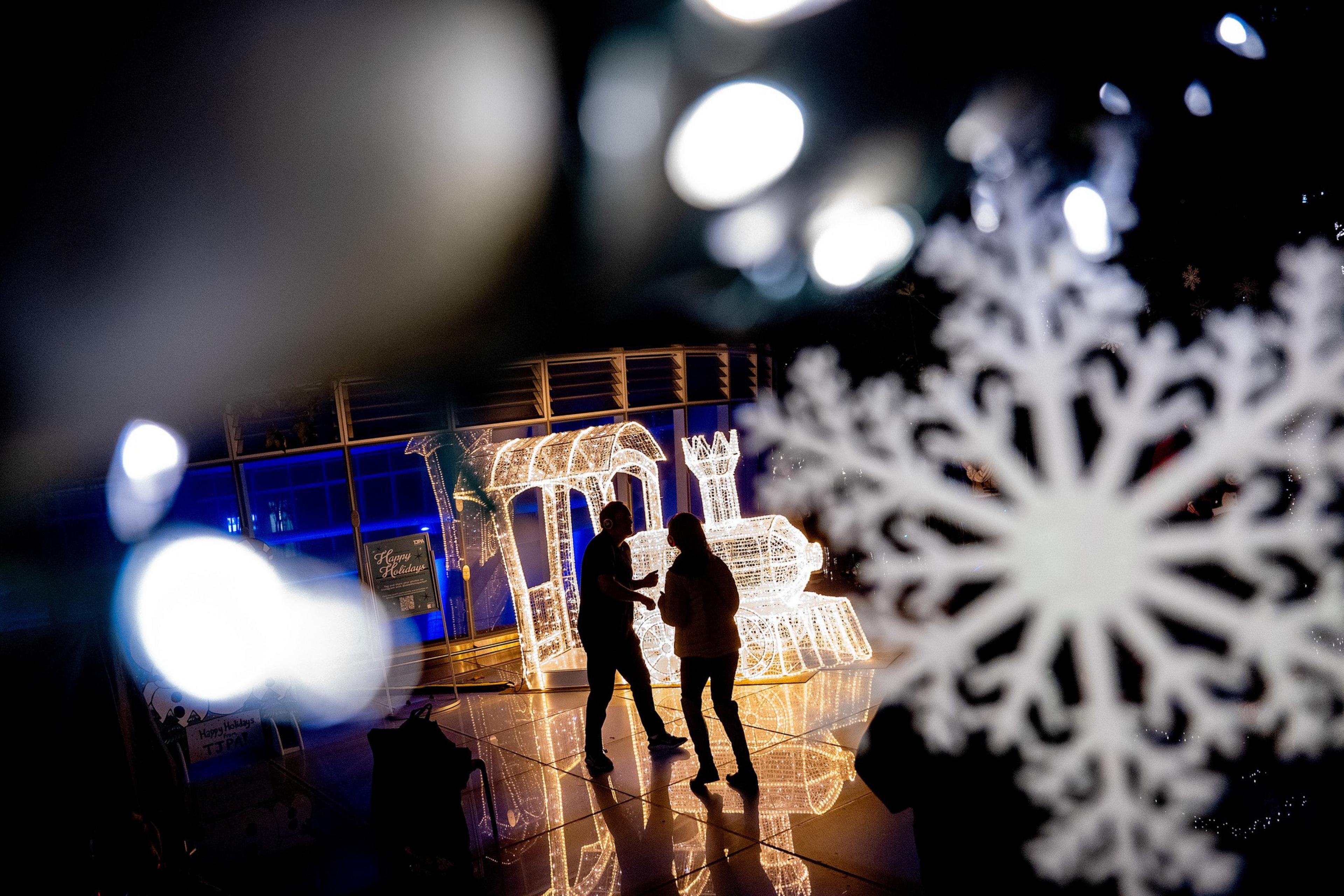 A festive scene shows two people silhouetted against a glowing train light display. A large decorative snowflake is in the foreground, creating a wintery atmosphere.