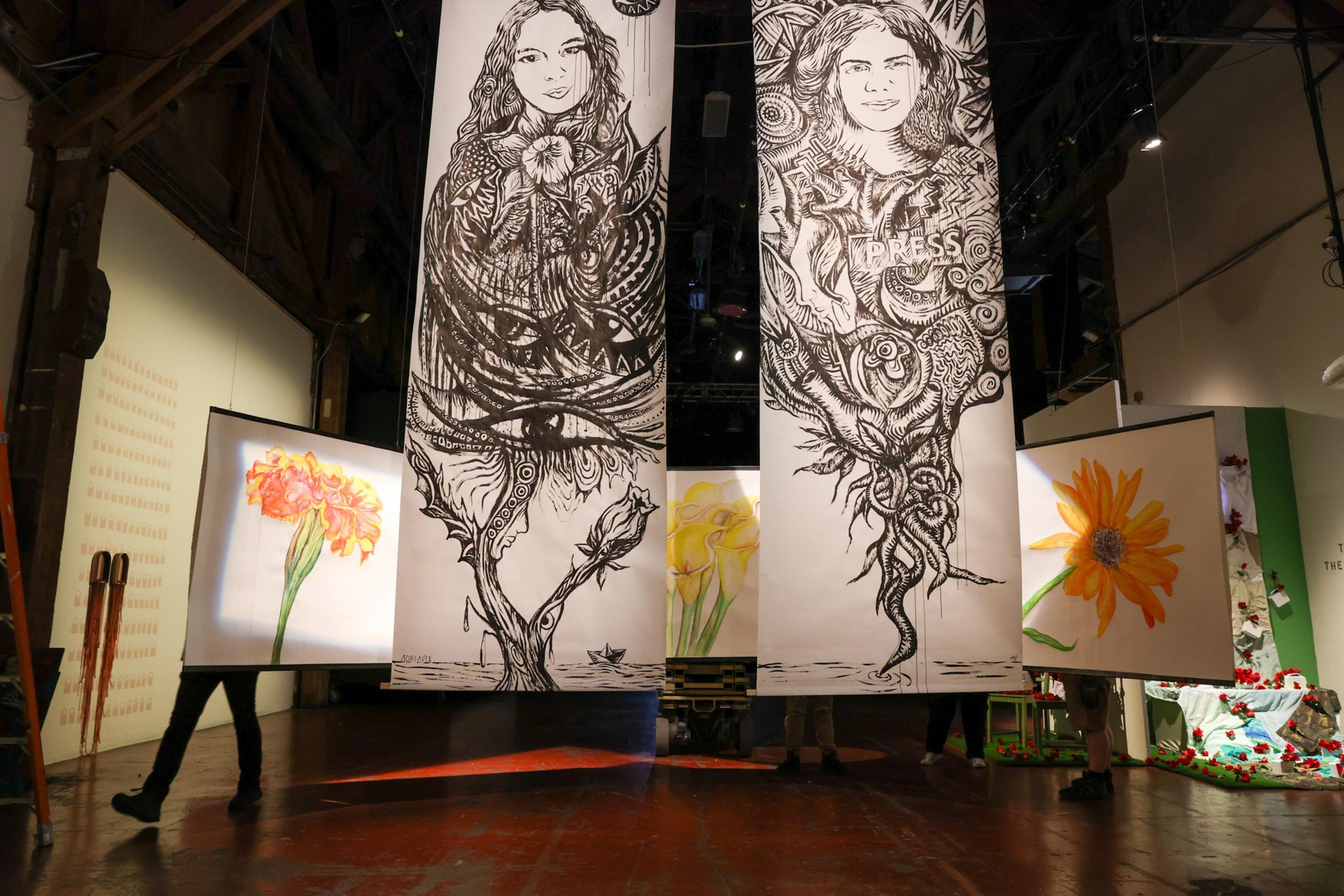 Large hanging panels feature two detailed black-and-white portraits with intricate designs and three colorful floral paintings on either side in a gallery space.