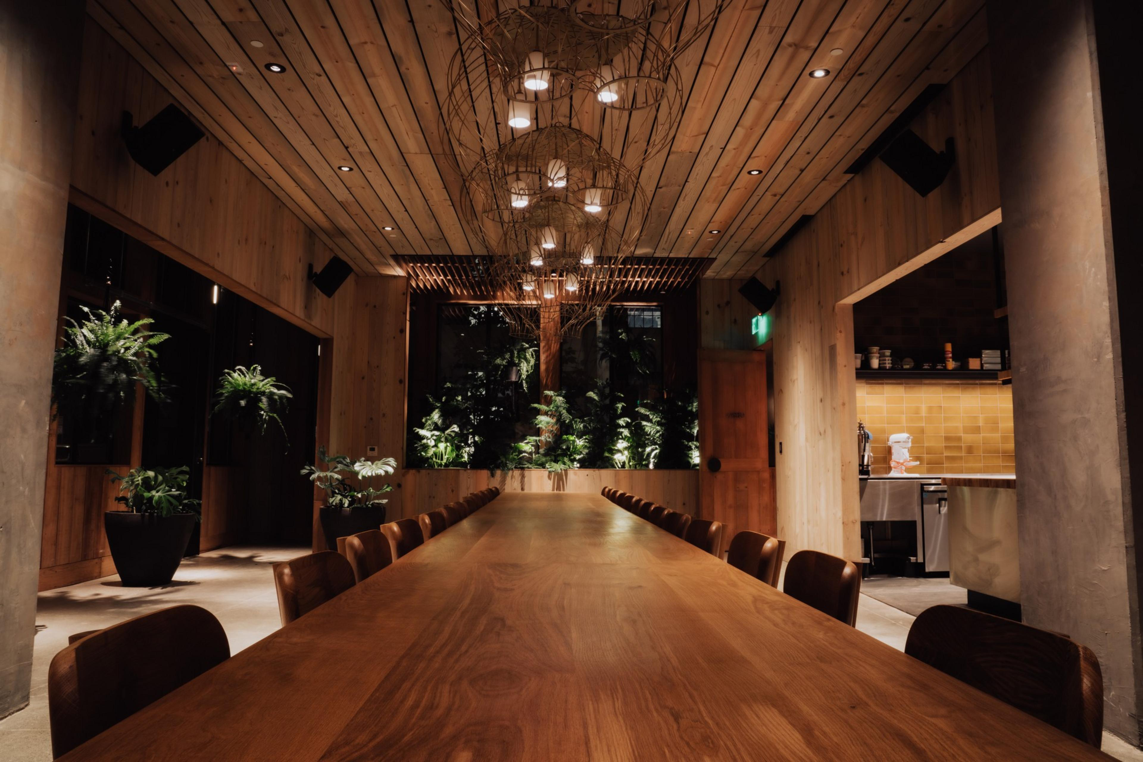 A long wooden table stands under a long light fixture.