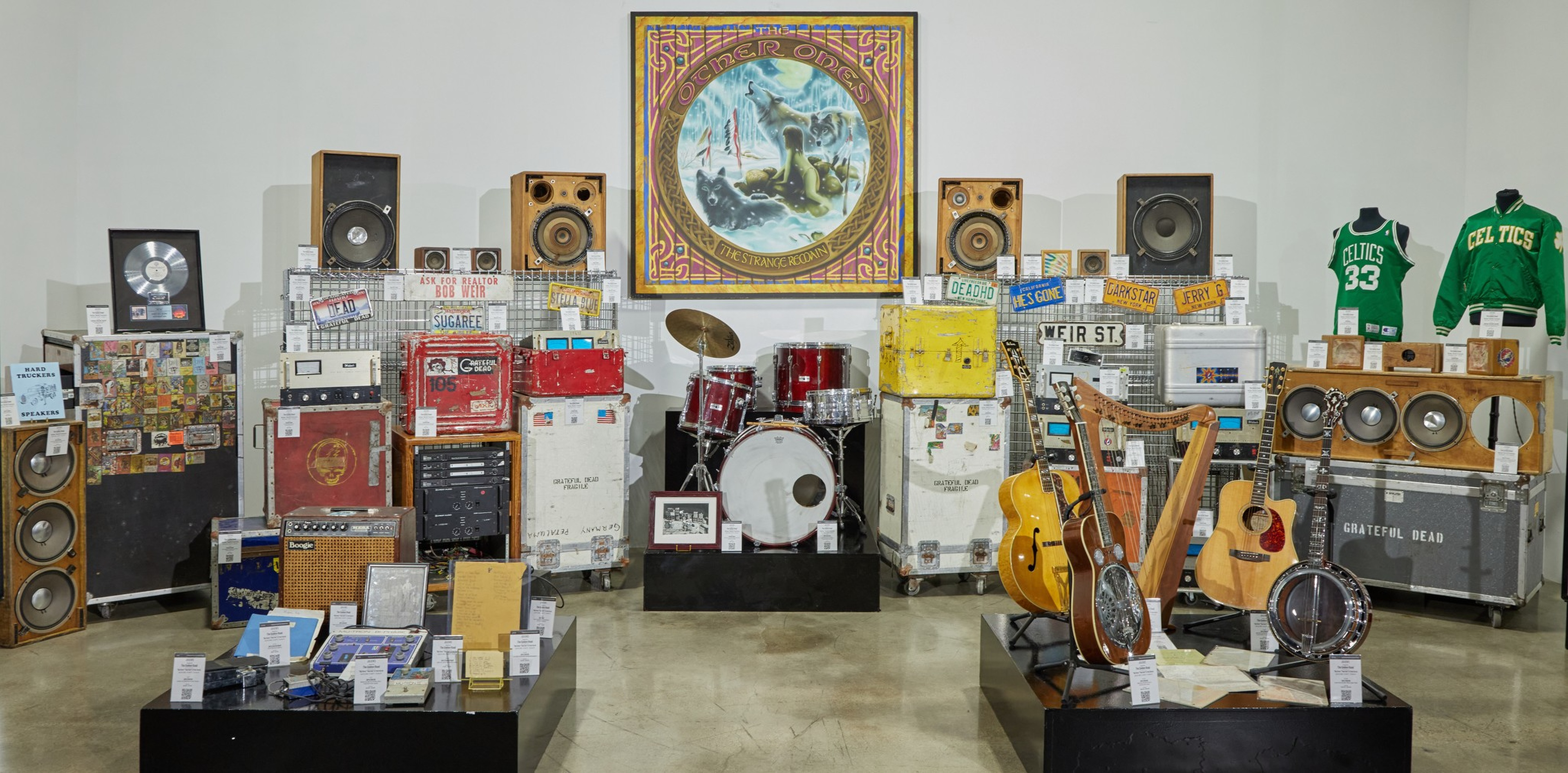A collection of vintage musical instruments, amplifiers, speakers, tour cases, and memorabilia, including drums, guitars, a harp, and two Celtics jerseys.
