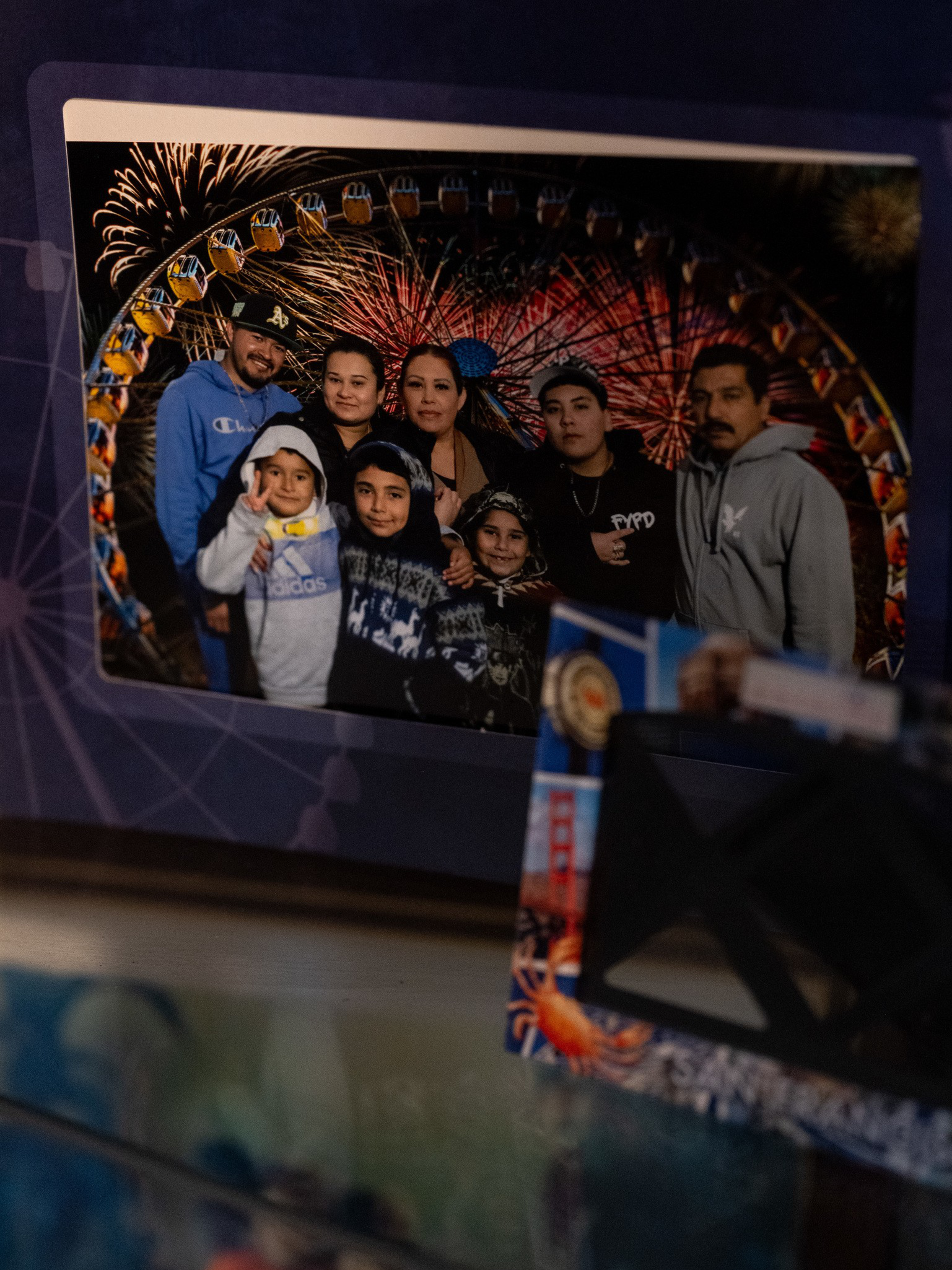 A group of seven people poses in front of a Ferris wheel with fireworks in the background, smiling and wearing casual clothing.
