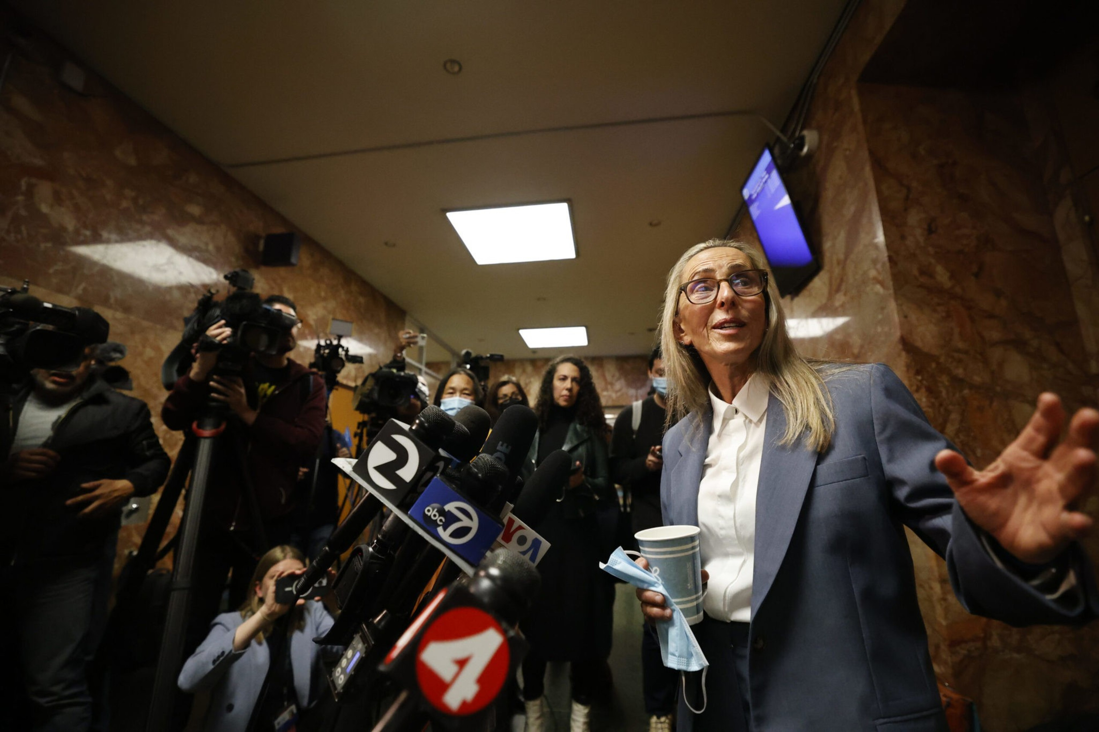A lawyer stands before news reporters in a hall.