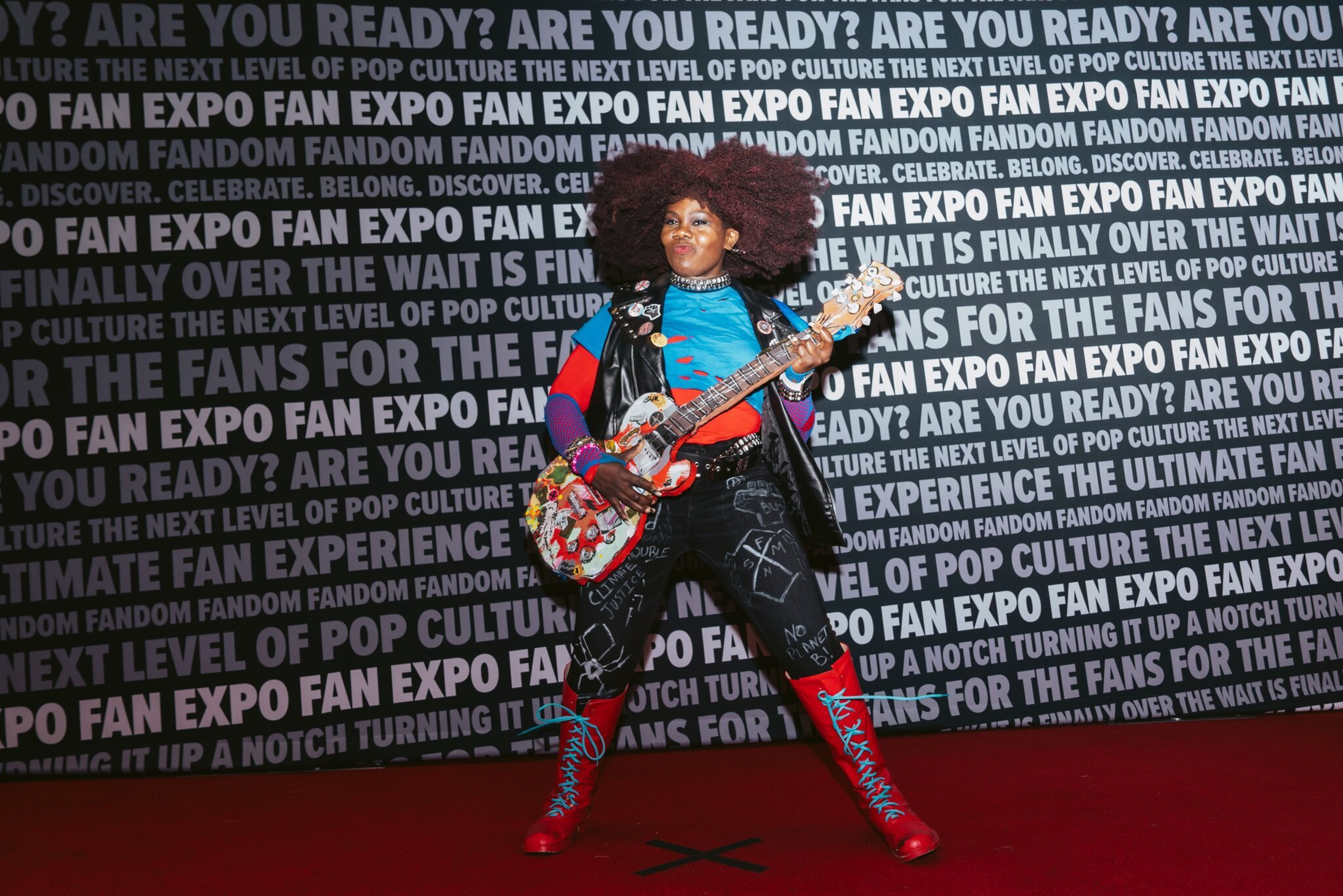 A woman holds a guitar in front of a step-and-repeat.