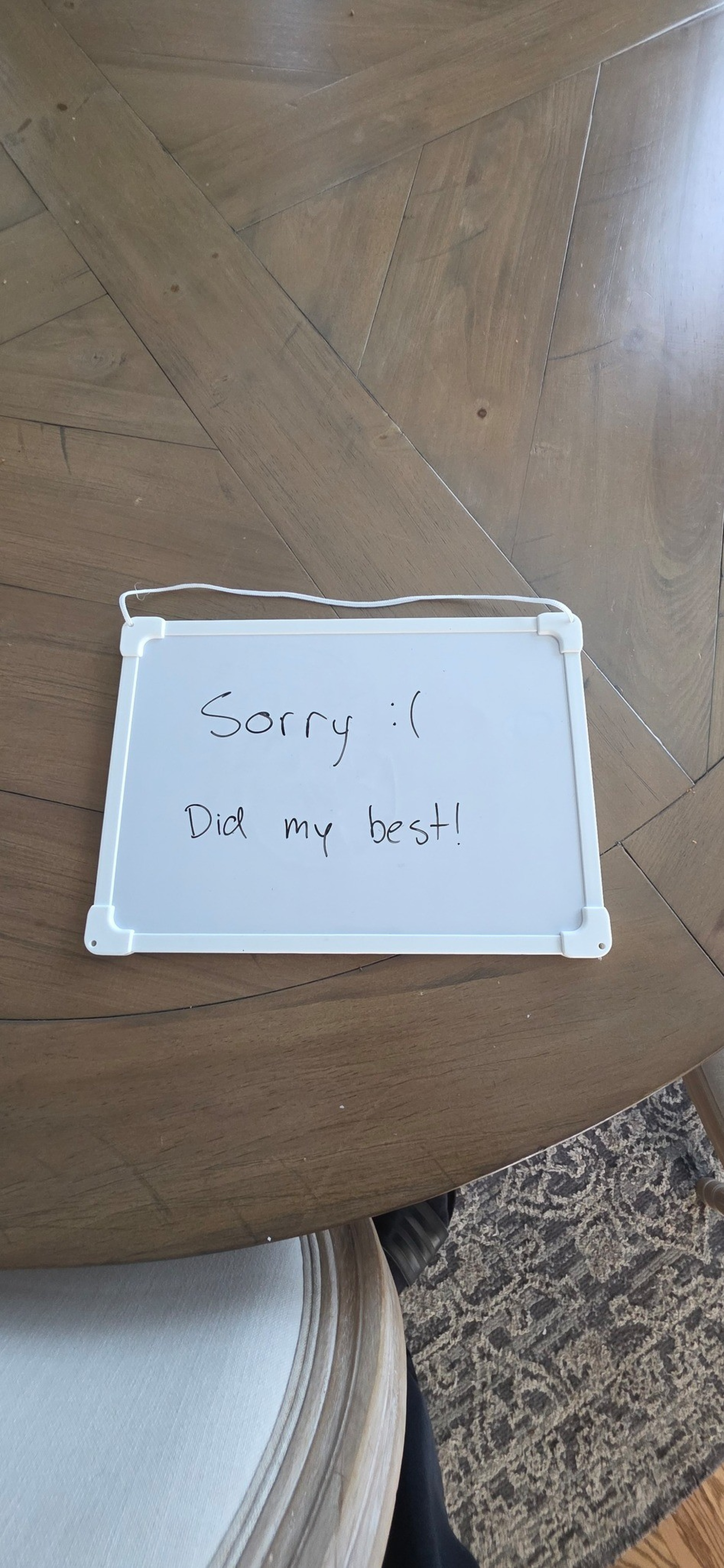 A small whiteboard on a wooden table reads, “Sorry :( Did my best!” with a slightly tilted placement.