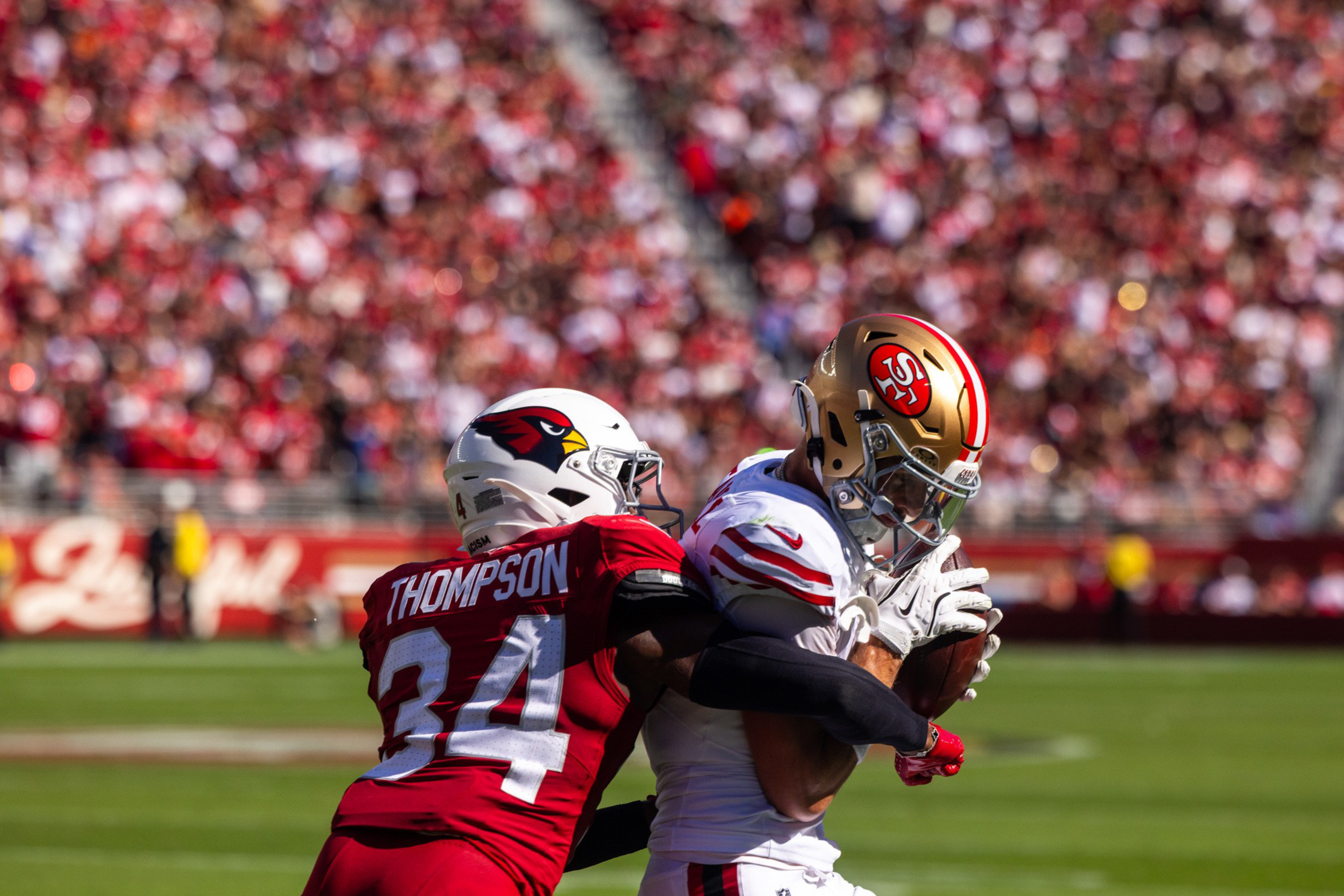 A football player from the Cardinals, wearing number 34, tackles a 49ers player holding the ball tightly during a game.