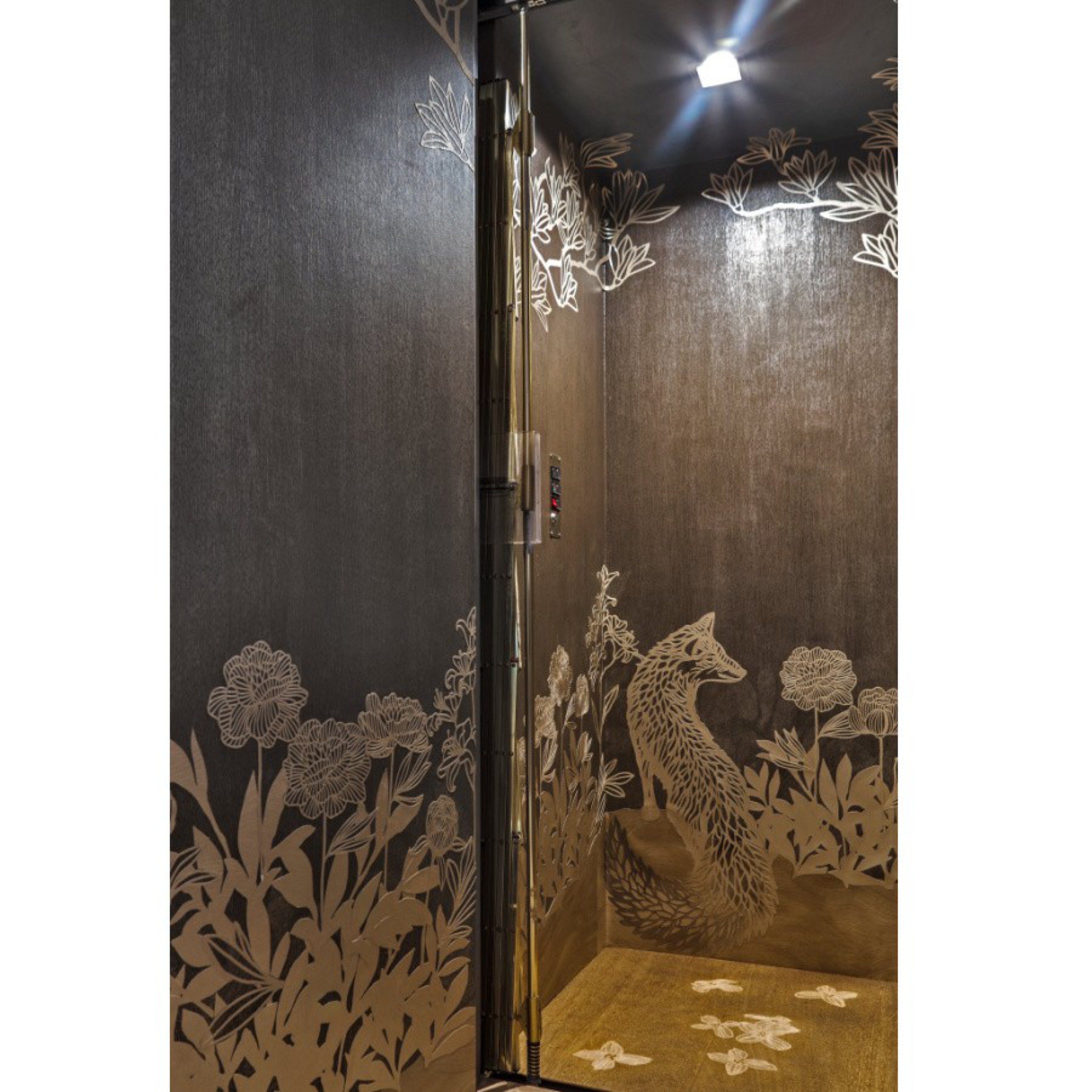 A dark elevator interior features metallic floral and leafy patterns with a detailed fox design sitting among the plants, illuminated by a ceiling light.