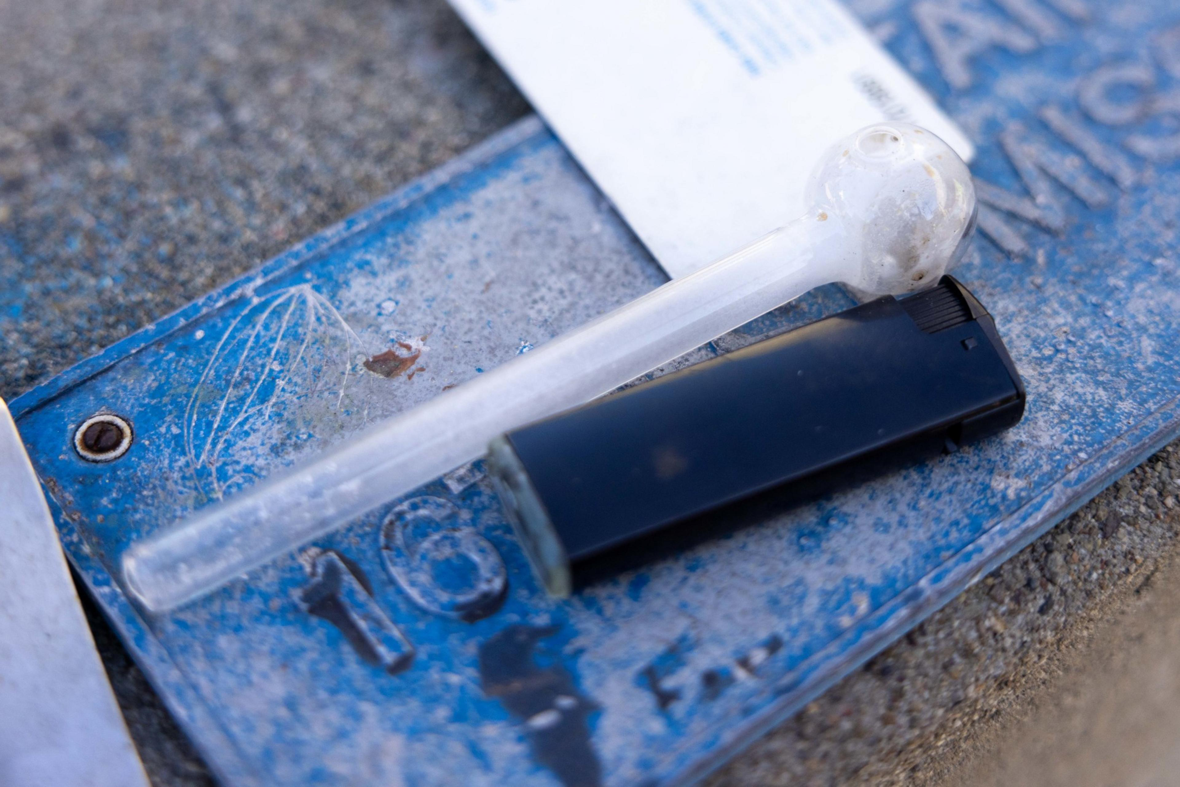 The image shows a glass pipe with residue, a black lighter, and a blue surface with numbers and text, indicating possible drug paraphernalia.