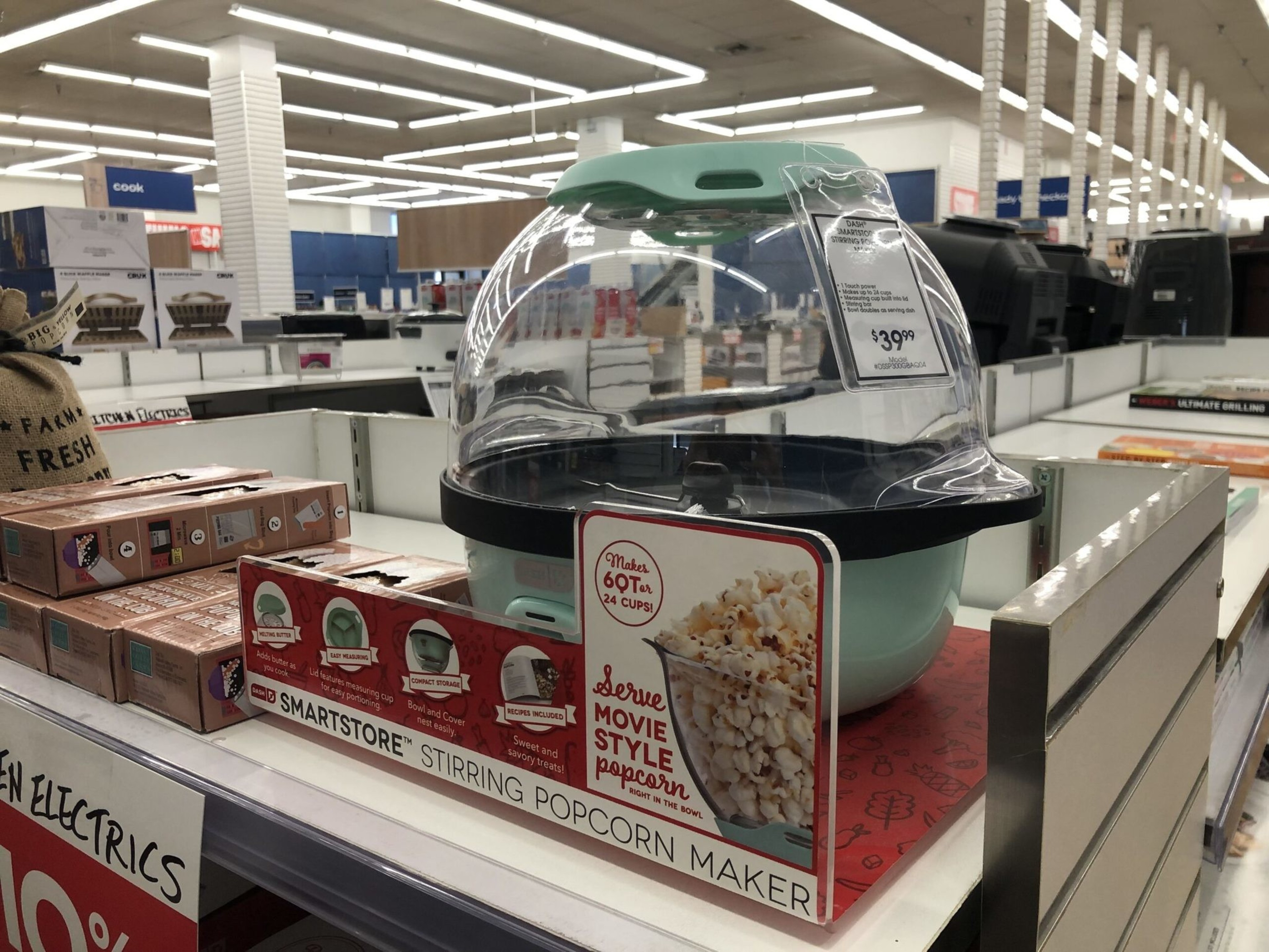 A mint green Smartstore stirring popcorn maker with a clear dome lid is displayed on a store shelf priced at $39.99.