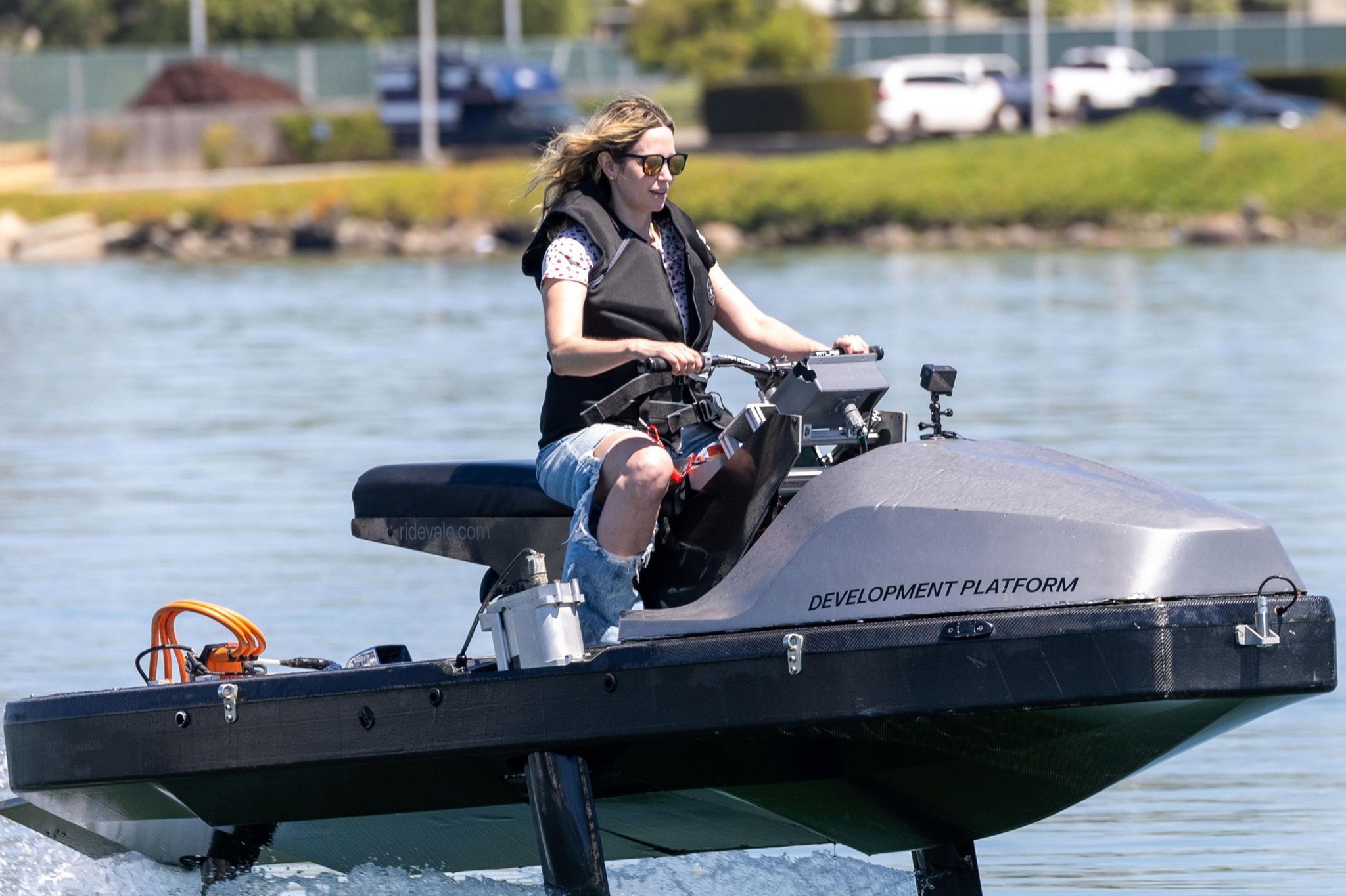 A person in sunglasses and a life jacket is riding a futuristic-looking watercraft labeled "DEVELOPMENT PLATFORM" on a calm body of water.