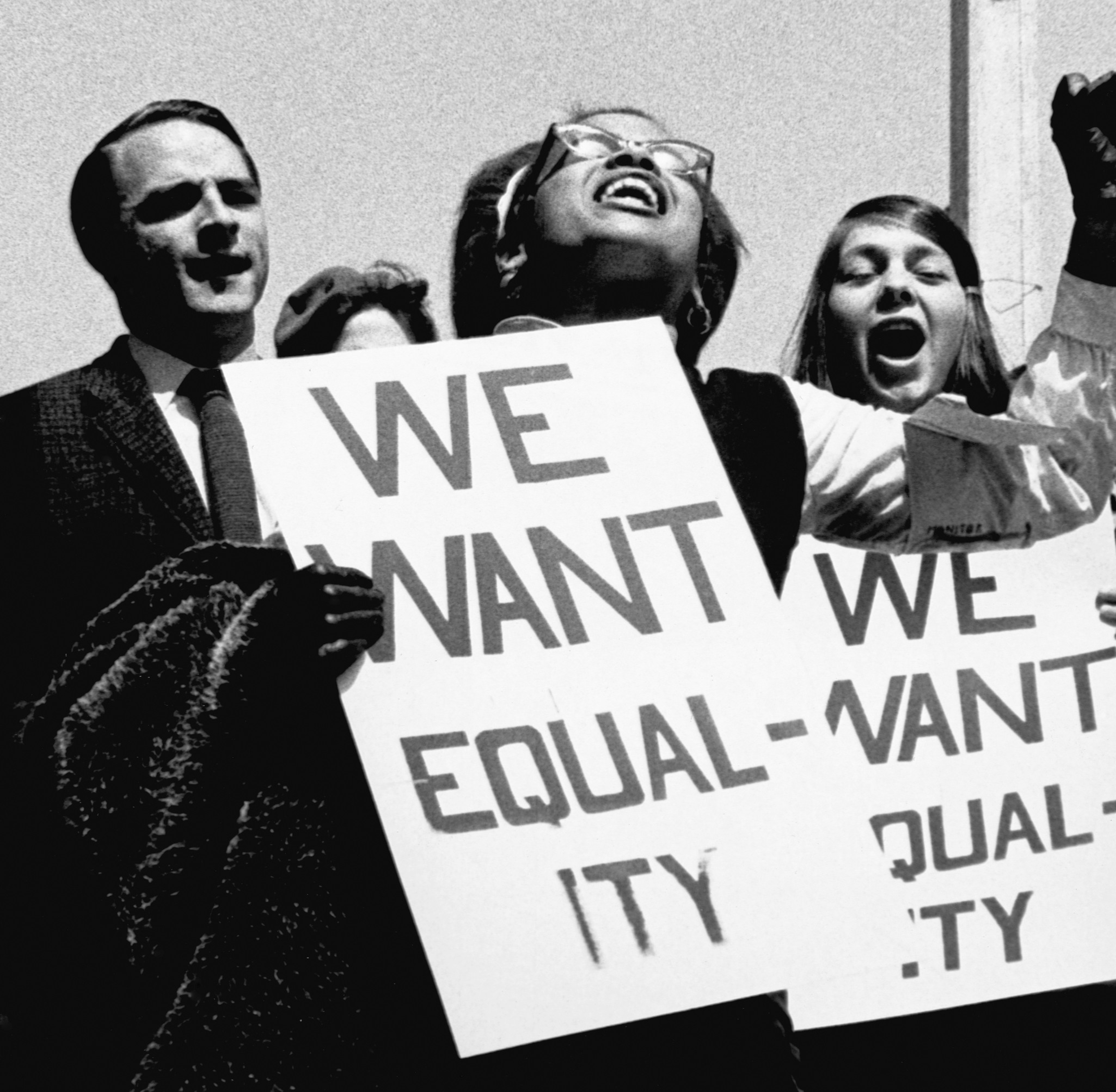 Two women and a man passionately hold signs reading "WE WANT EQUALITY" during a protest, with the women visibly shouting or chanting.