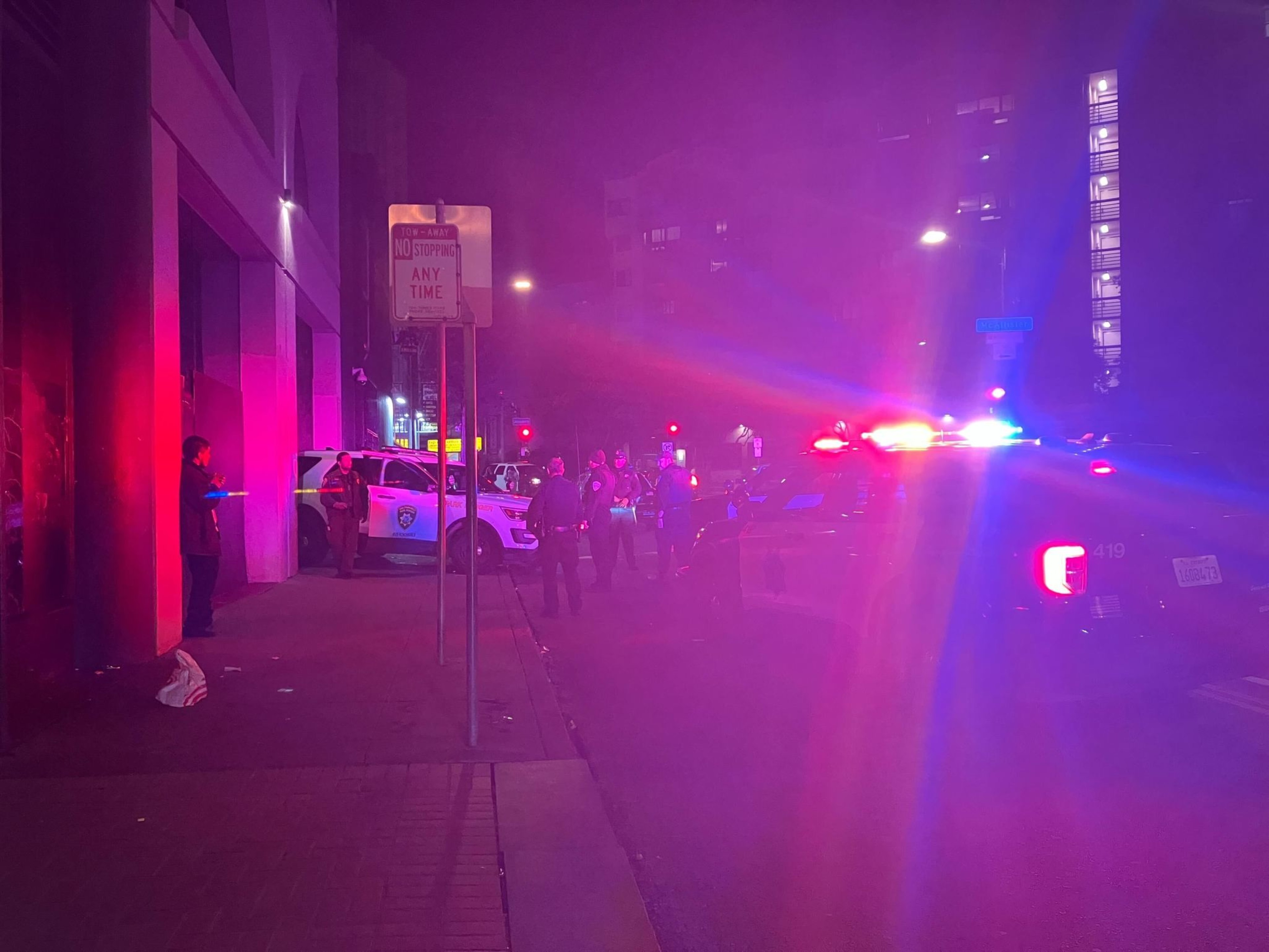 An SUV backed into a building rests on a sidewalk, with police officers investigating.