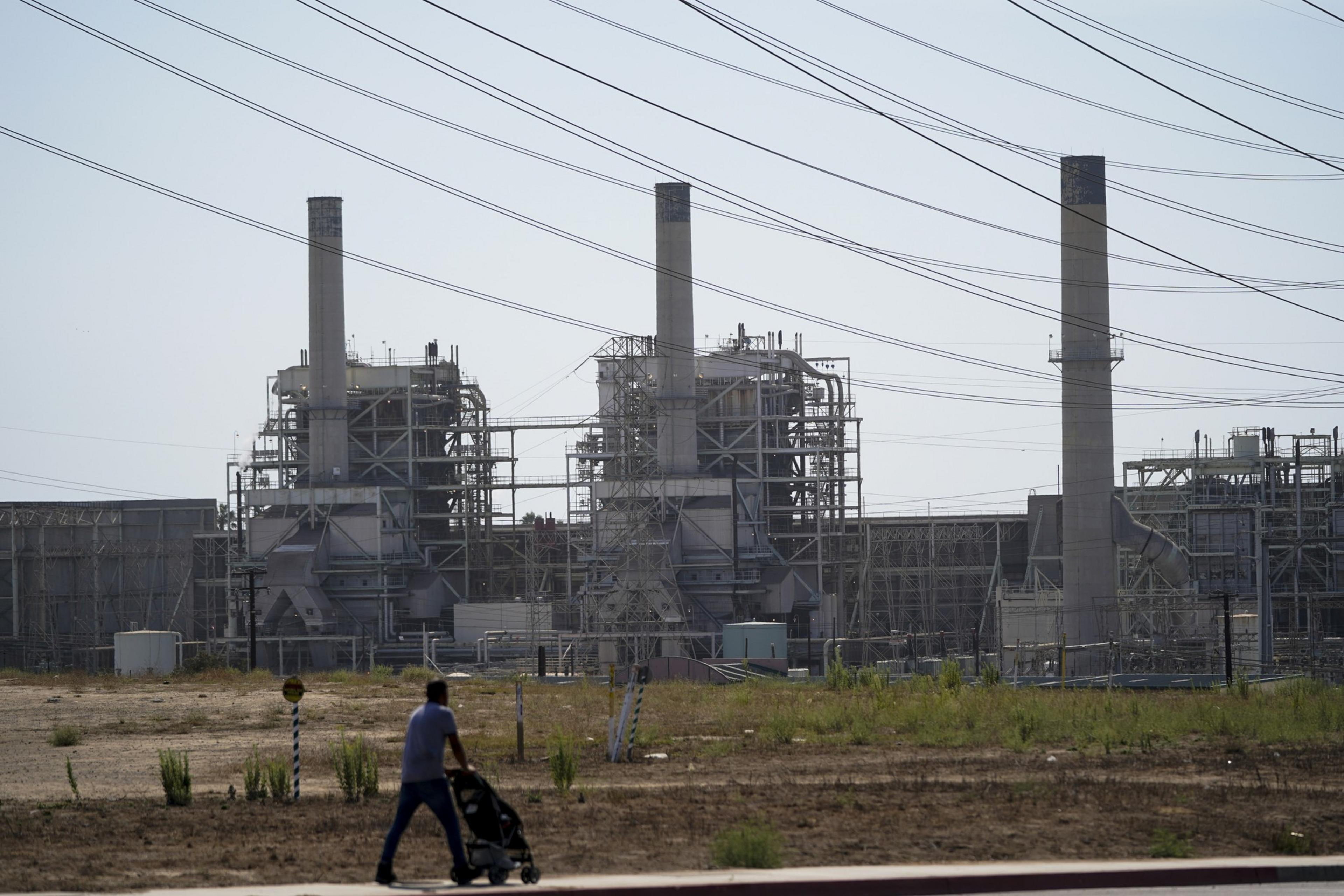 A person pushes a stroller past industrial buildings with tall chimneys and power lines.