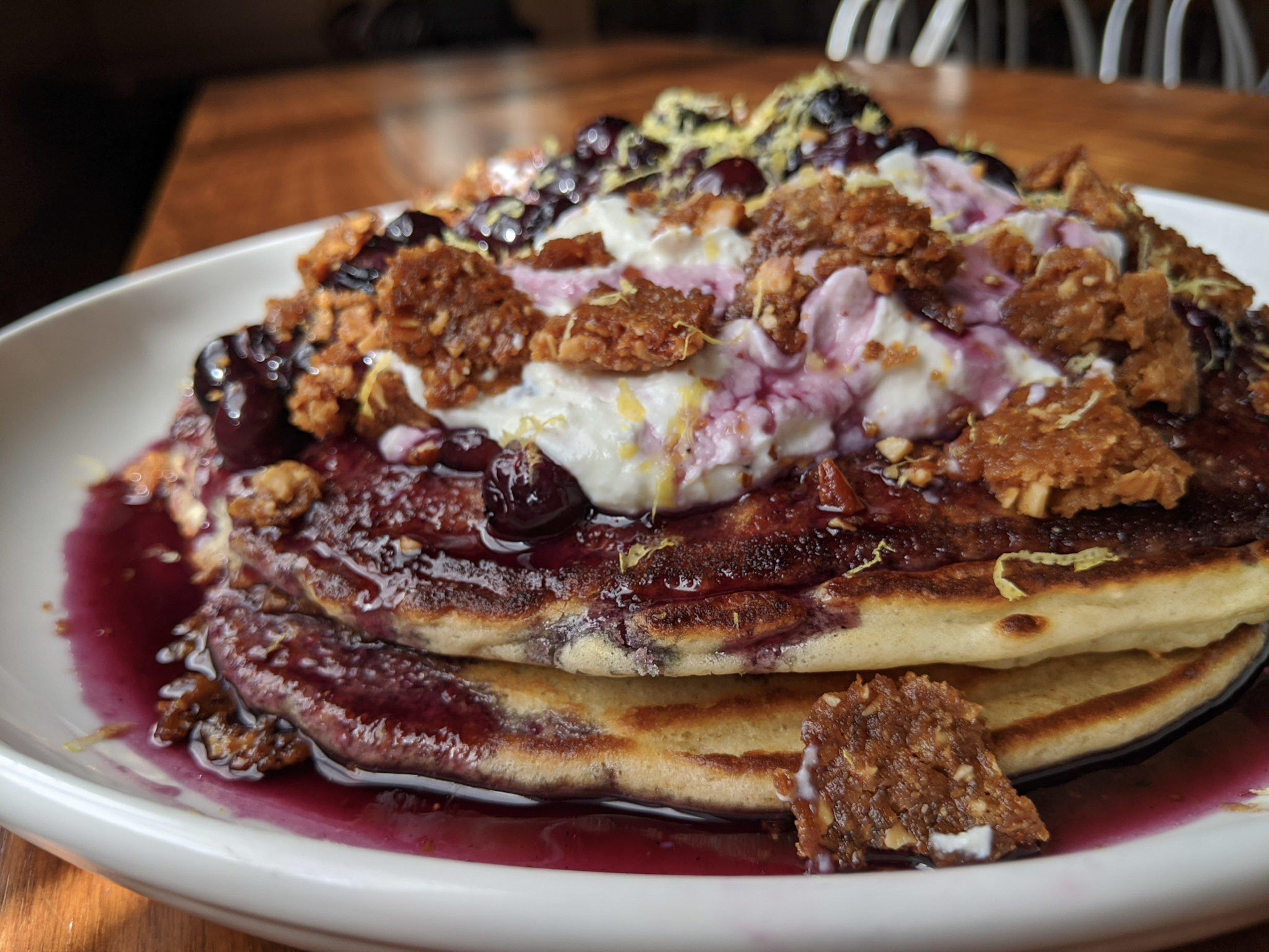 Bananas foster pancakes, with caramelized bananas flamed in spiced rum and ladled over banana-walnut hot cakes, then finished with toasted coconut cream and maple syrup, rest on a plate atop a table.