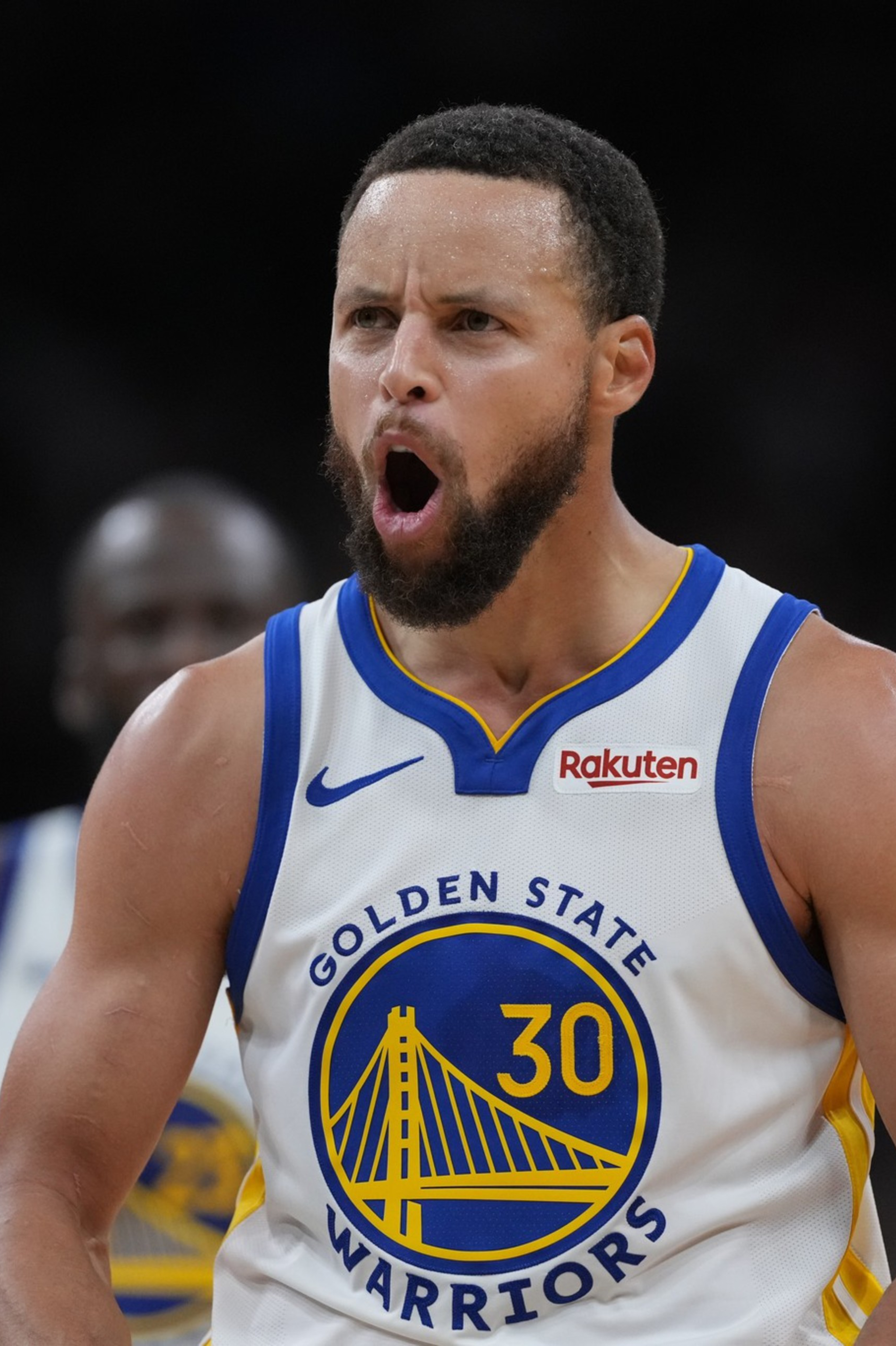 A basketball player wearing a white Golden State Warriors jersey with number 30 shouts, showing intense emotion on the court.