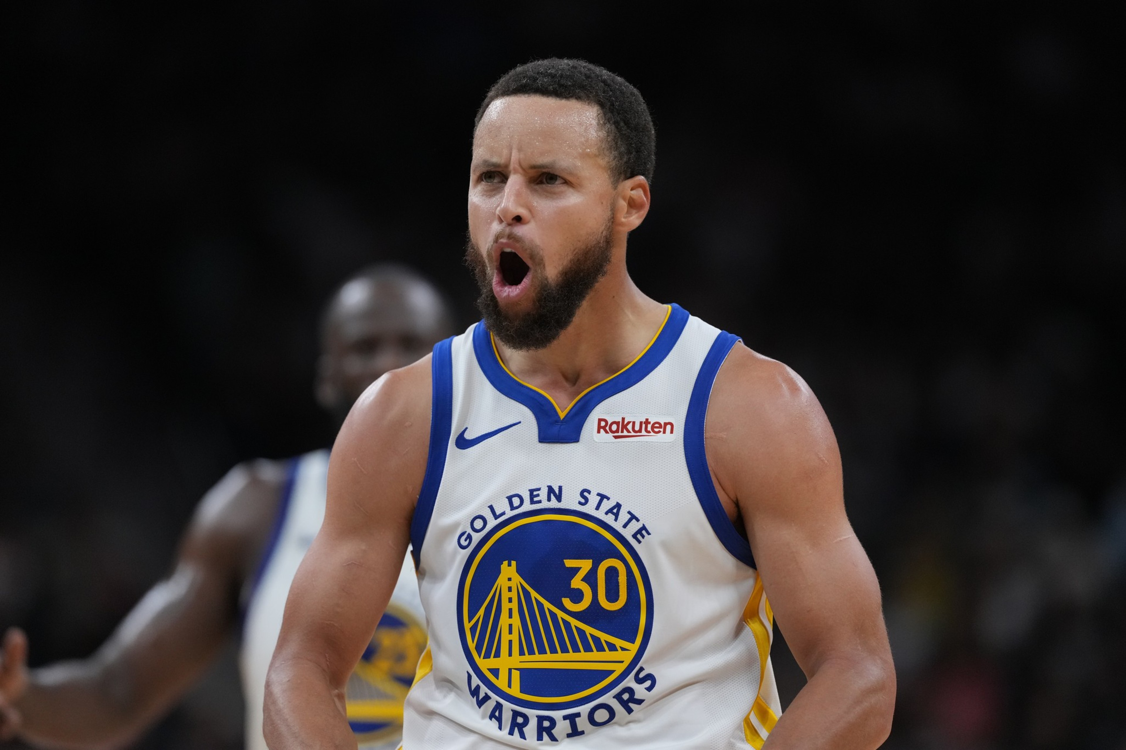 A basketball player wearing a white Golden State Warriors jersey with number 30 shouts, showing intense emotion on the court.