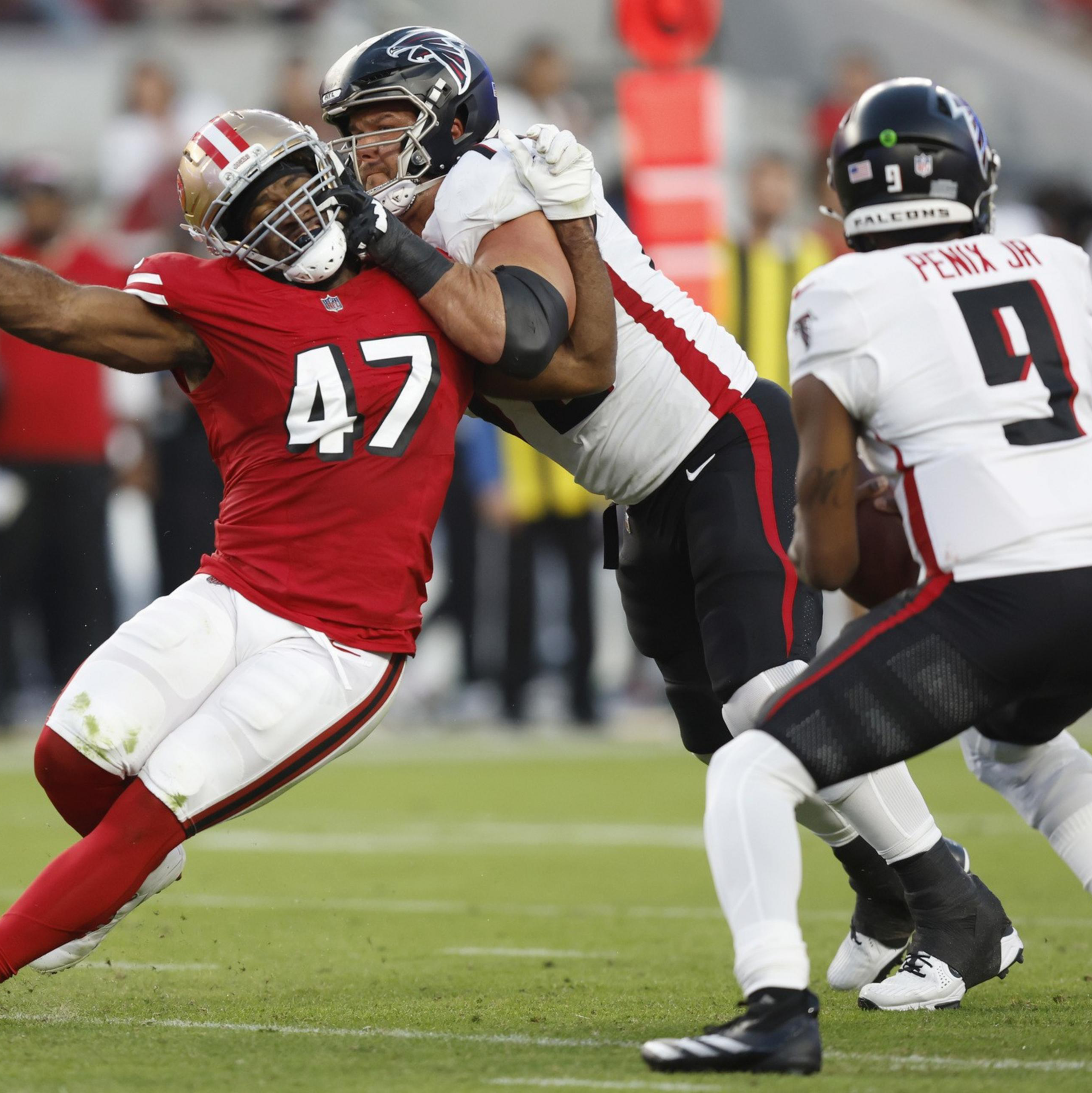 A San Francisco 49ers player wearing number 47 is being blocked by an Atlanta Falcons player while the Falcons quarterback, number 9, prepares to throw the ball.