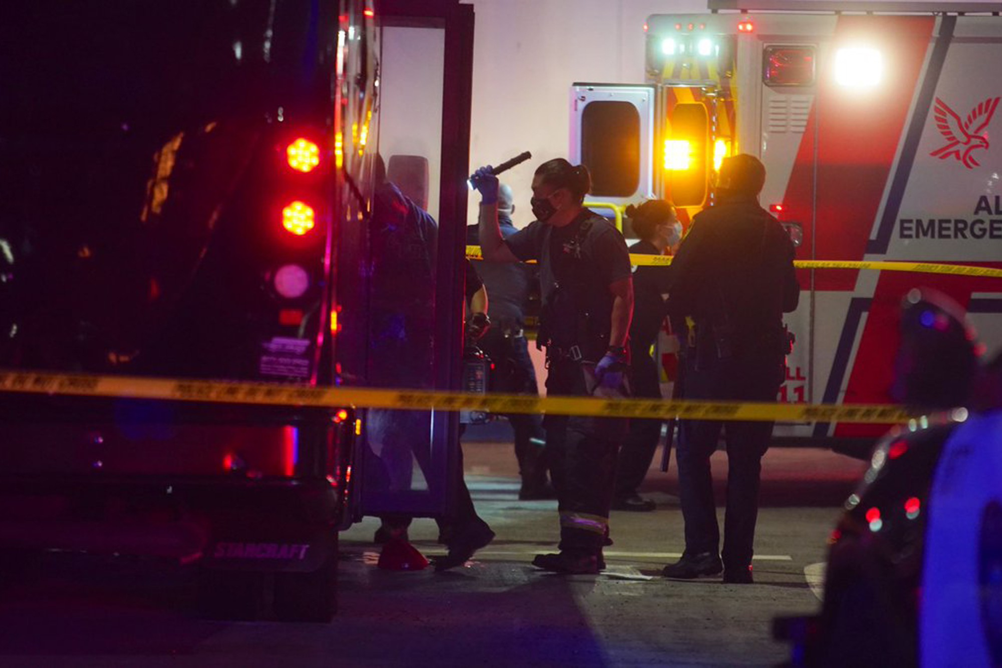 Emergency vehicles and personnel behind yellow tape at a nighttime incident scene.