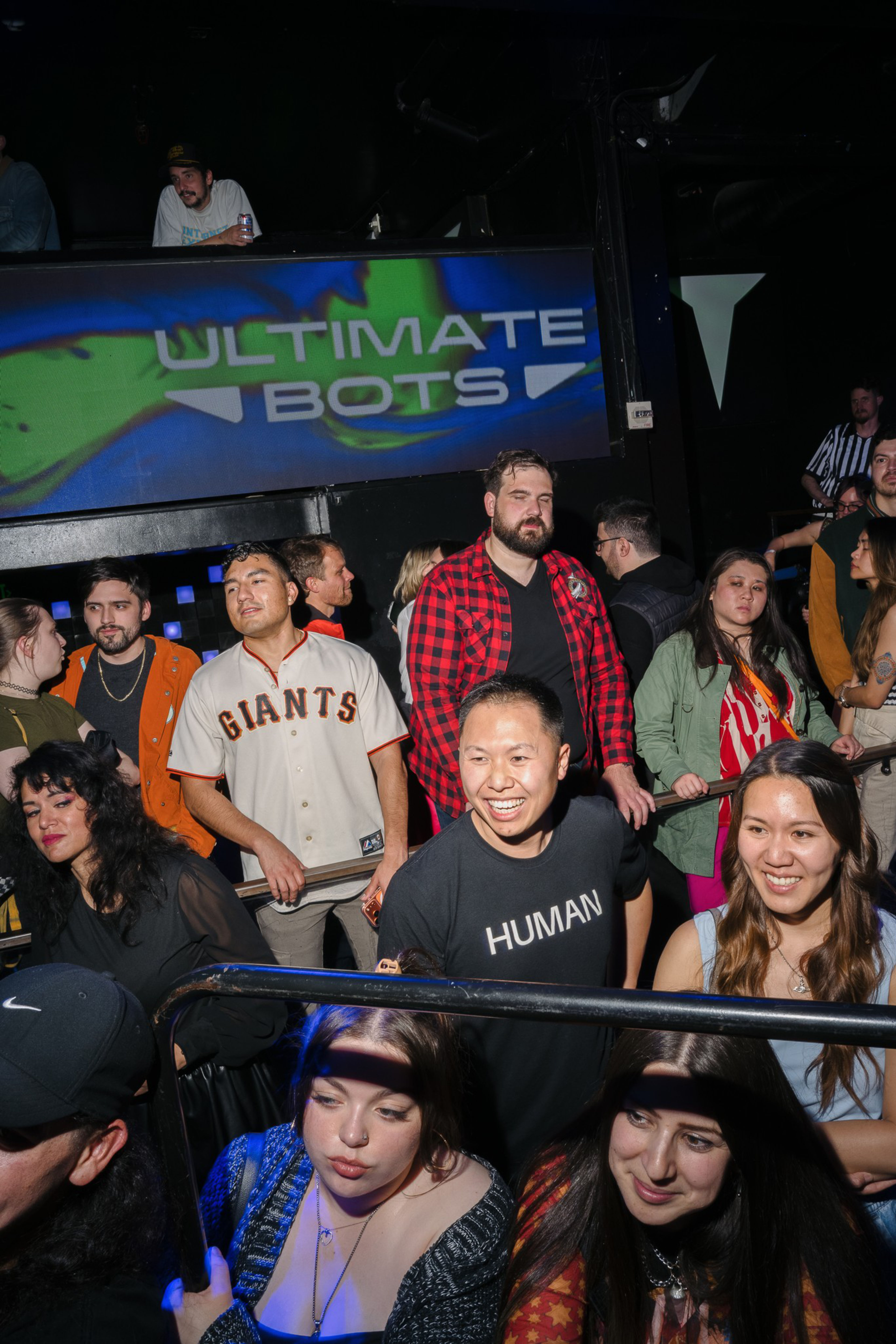 A diverse group of people stand and smile at an event, with a large sign reading “ULTIMATE BOTS” in the background.