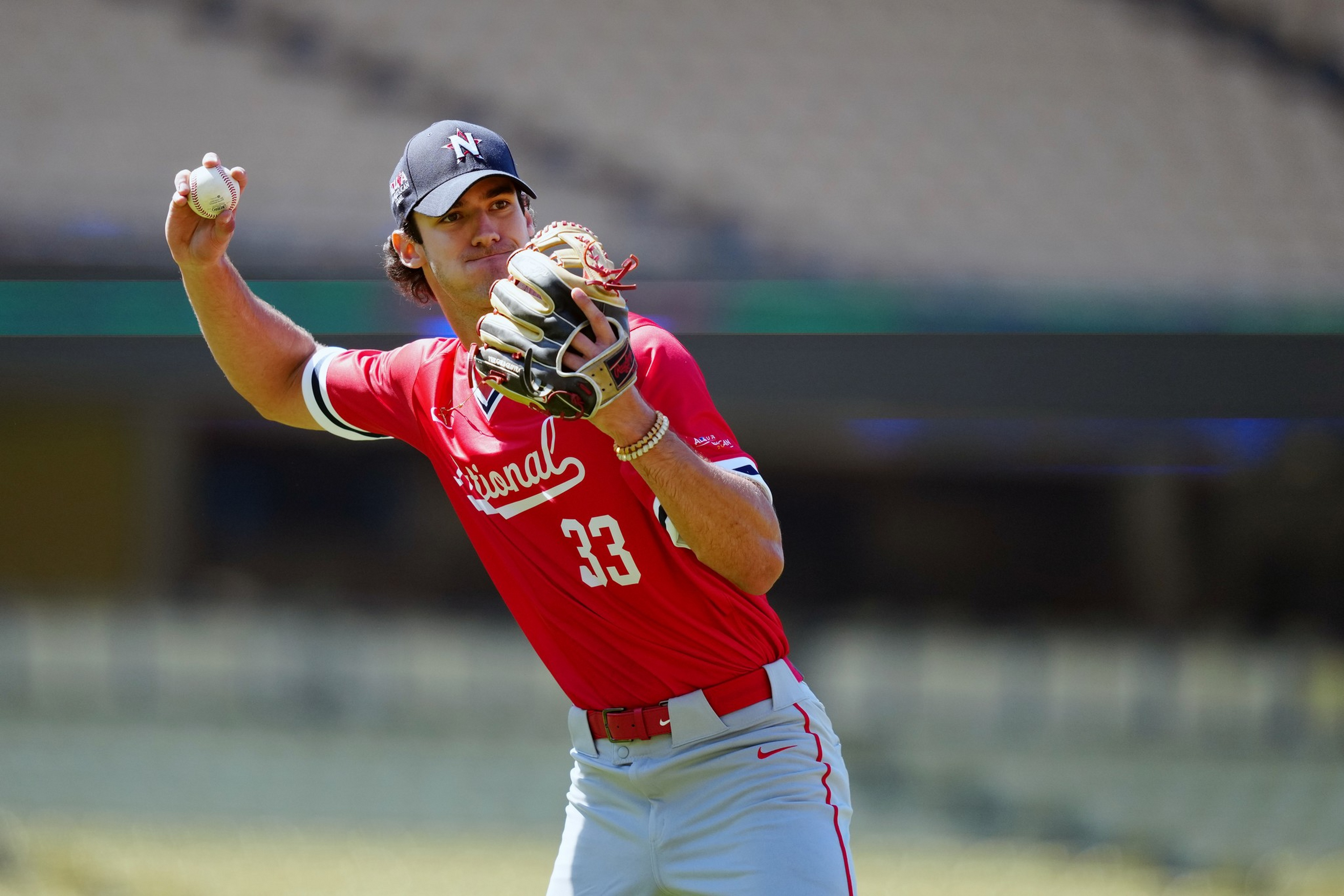 A baseball player in a red jersey and gray pants prepares to throw a ball, wearing a black cap and a glove on his left hand.