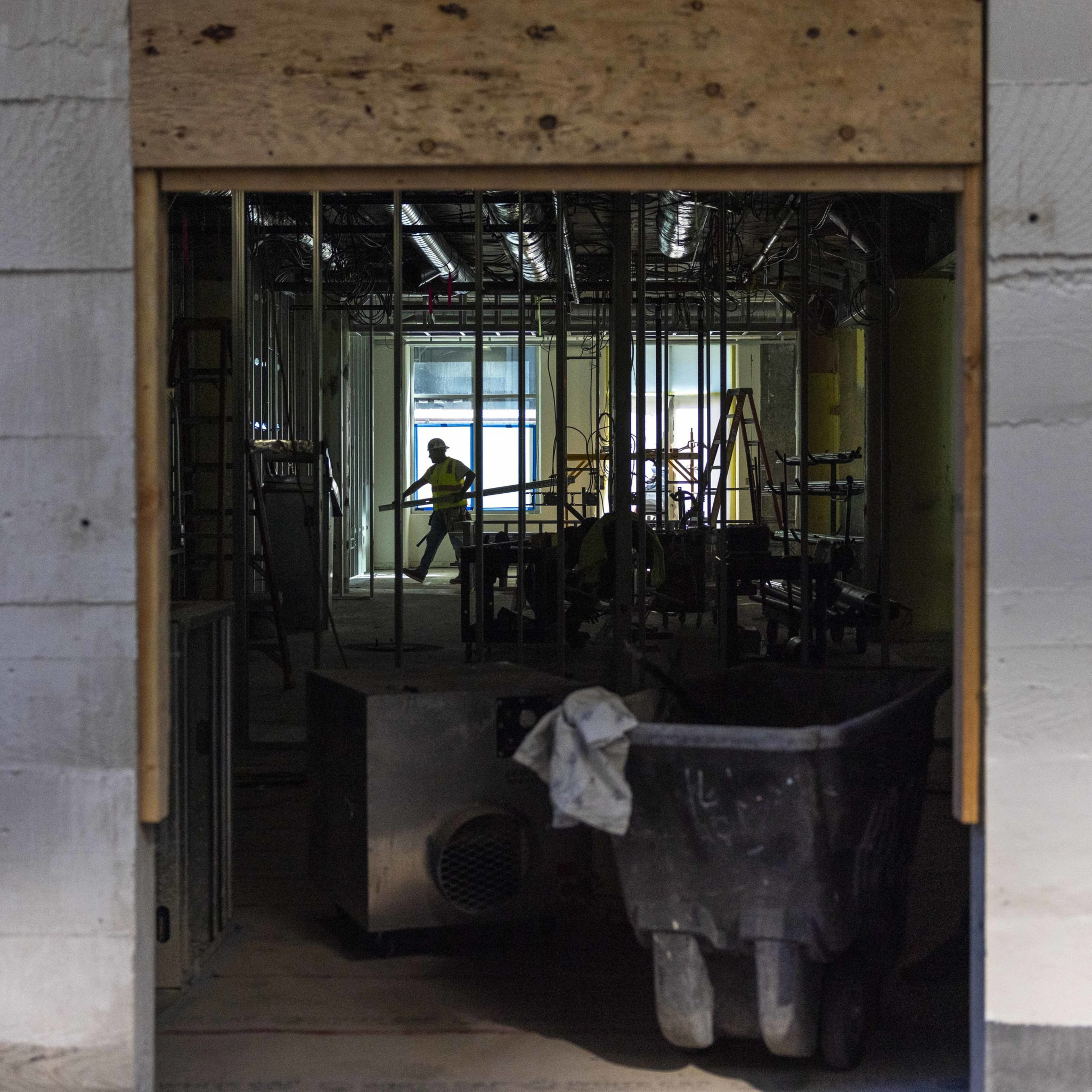 The image shows a dimly lit construction site with exposed framework and scattered equipment. A worker in a hard hat is illuminated near a distant window.