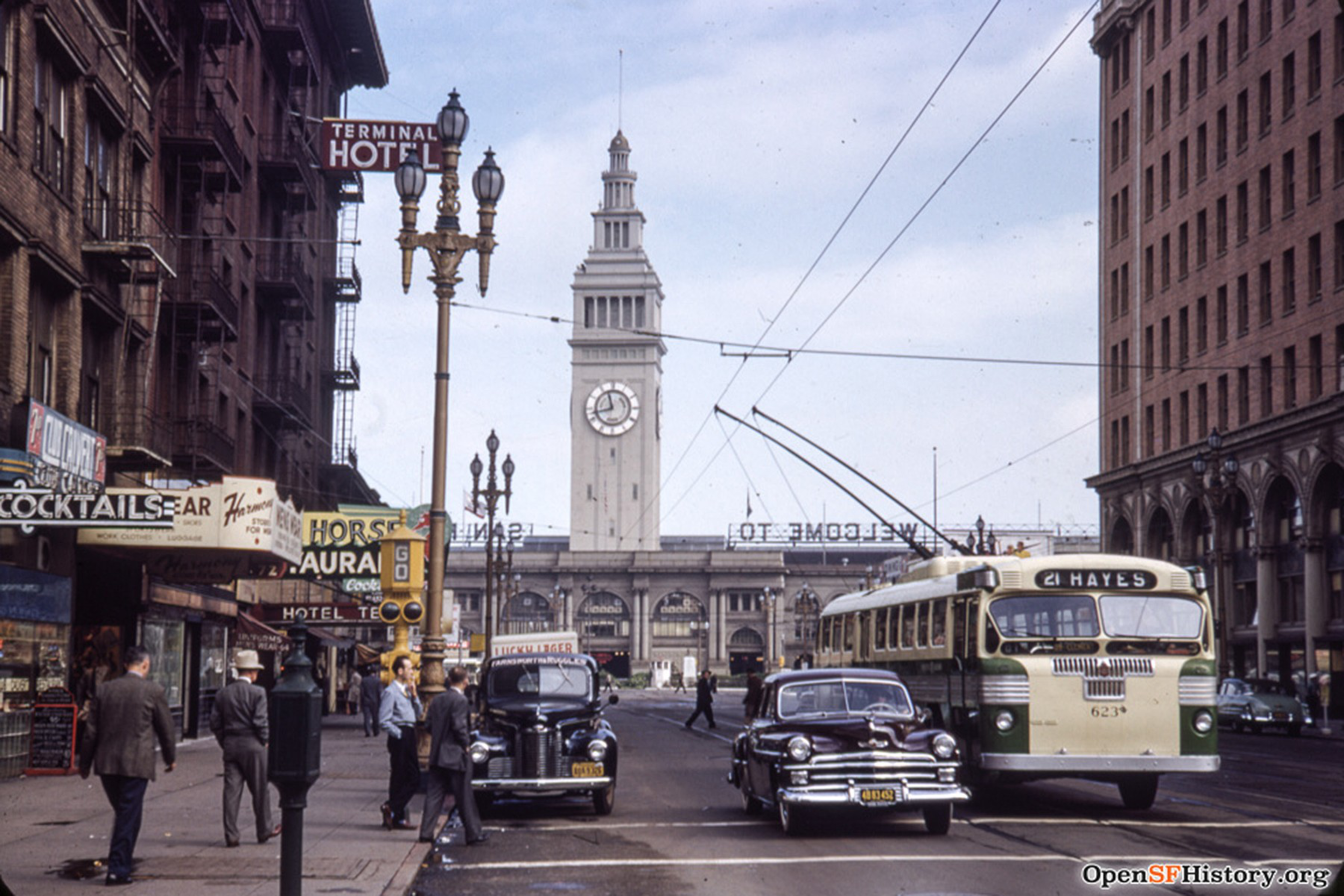 A archival photo of a screets scene on Market Street that includes cars from the 1950s and the SF Ferry Building