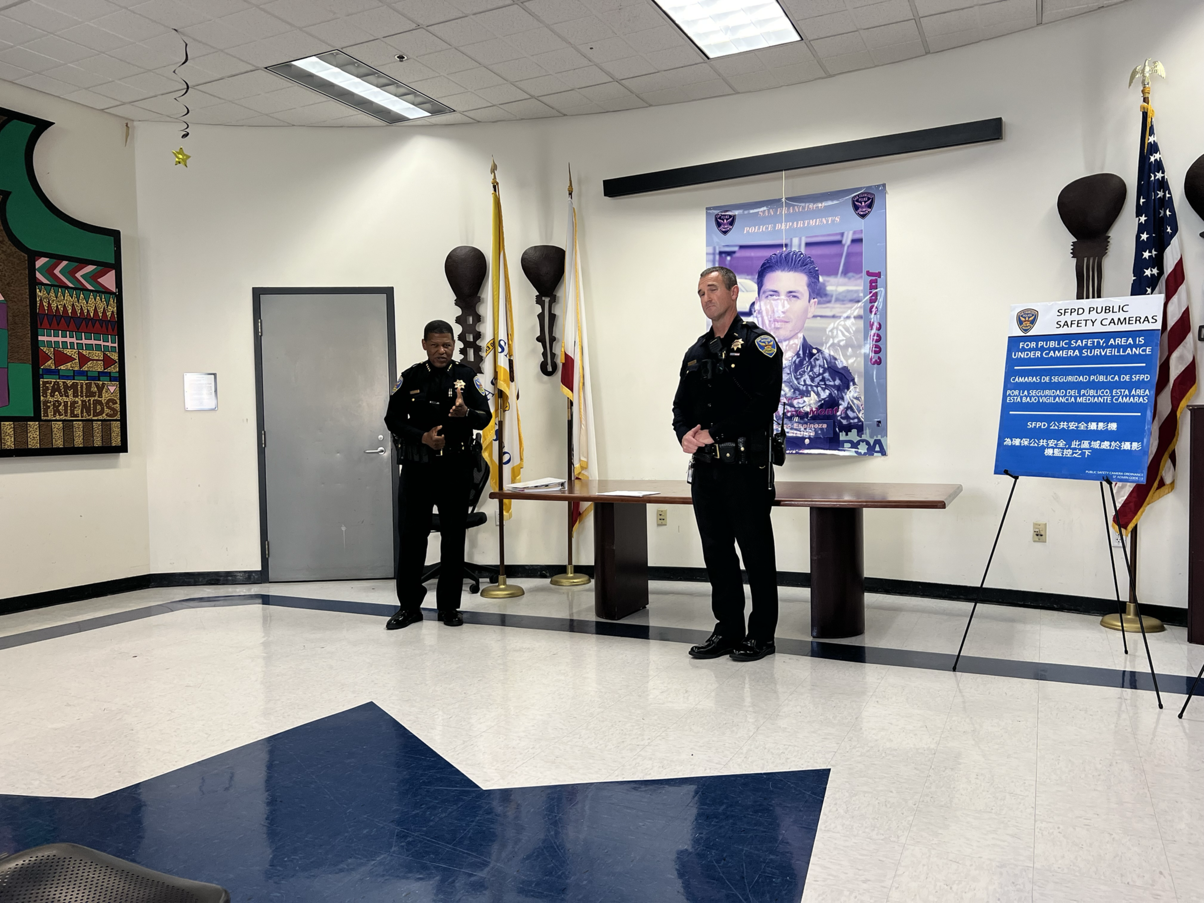 Two police officers stand at the front of a meeting hall.
