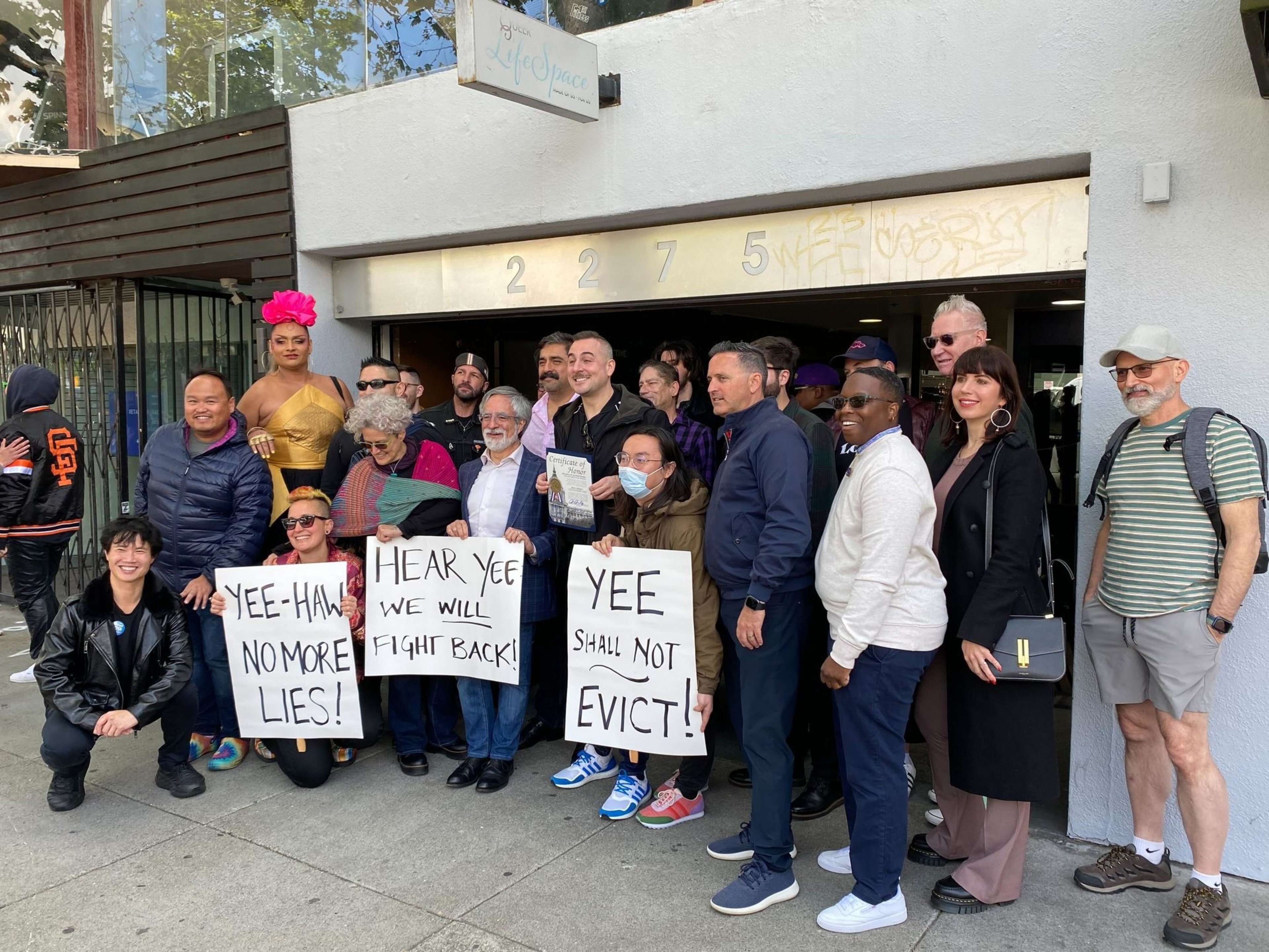 A diverse group of people stand in front of a building, holding signs with messages like &quot;No more lies!&quot; and &quot;We will fight back!&quot;