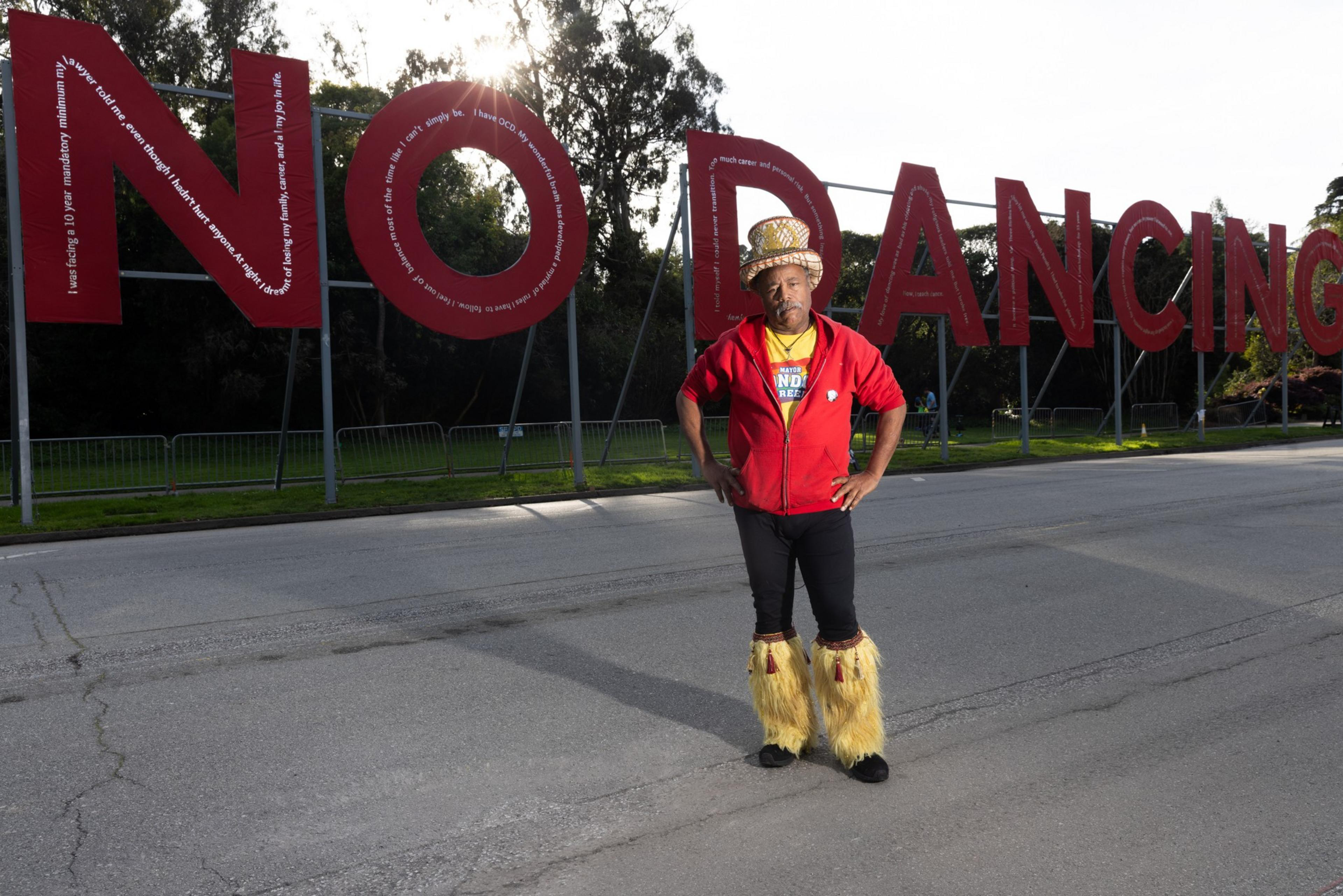 A person with a top hat and red sweater stands with a &quot;No Dancing&quot; sign in the back.