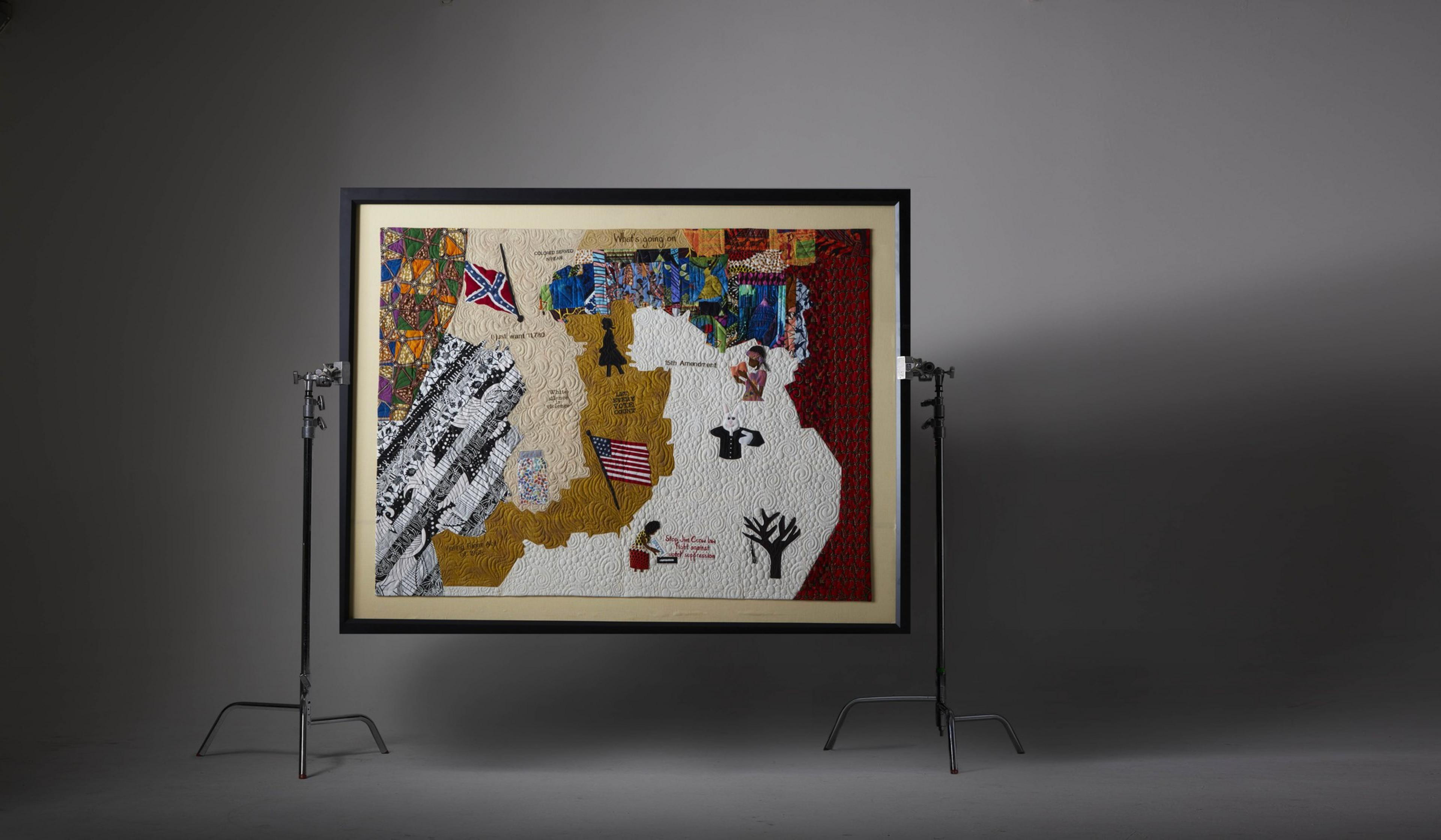 A quilt filled with political motifs from the Jim Crow era including the Confederate flag, hangs from a rack.