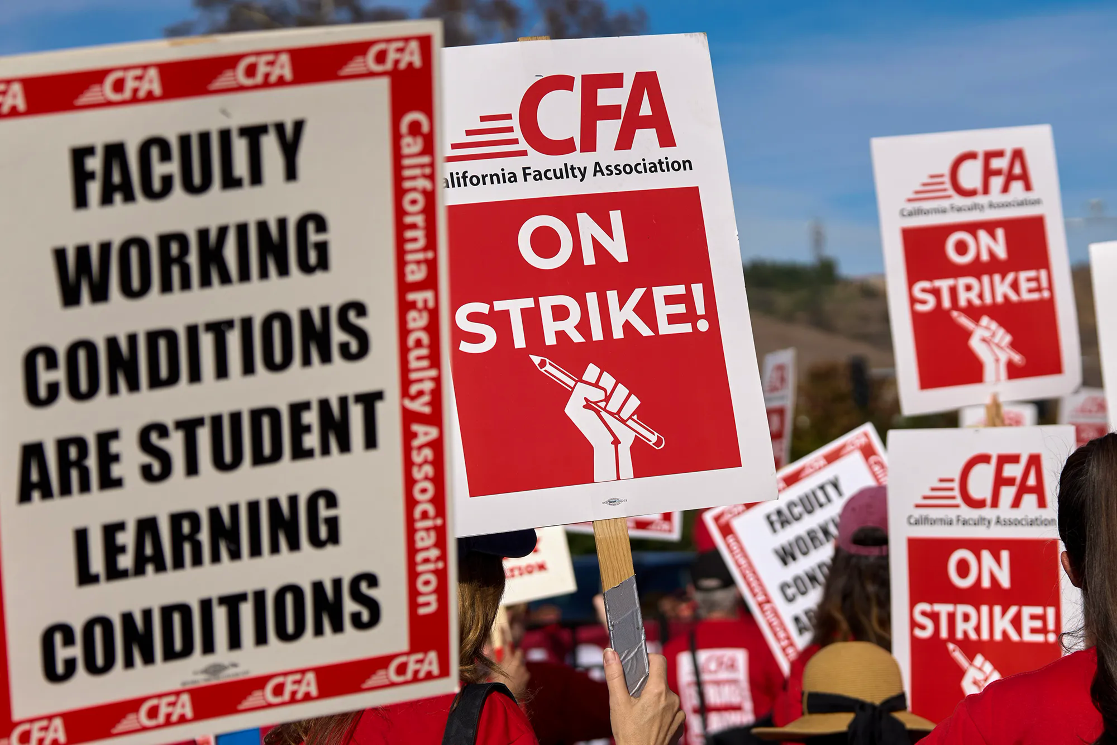 People in red are holding signs saying "Faculty working conditions are student learning conditions" and "CFA On Strike!"
