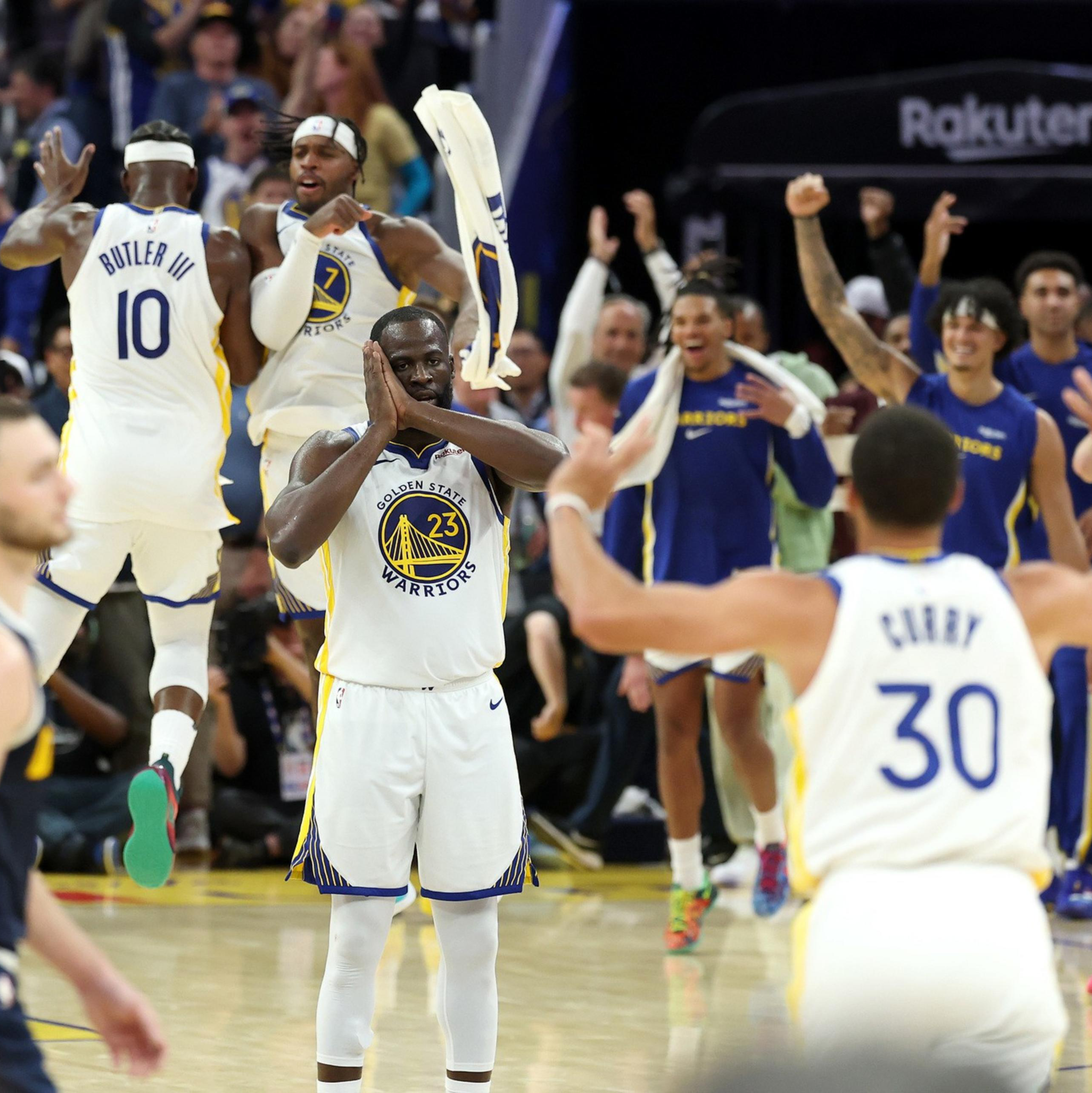 Golden State Warriors players celebrate on the court, with one player clapping hands and others cheering excitedly in the background.